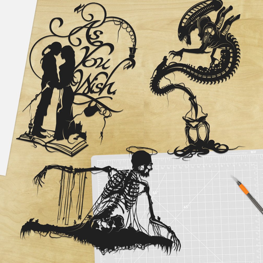 Will Pigg hand cut paper Silhouettes of a romantic couple, a dragon, and a skeleton practicing yoga on a wooden surface with a cutting mat and craft knife nearby.