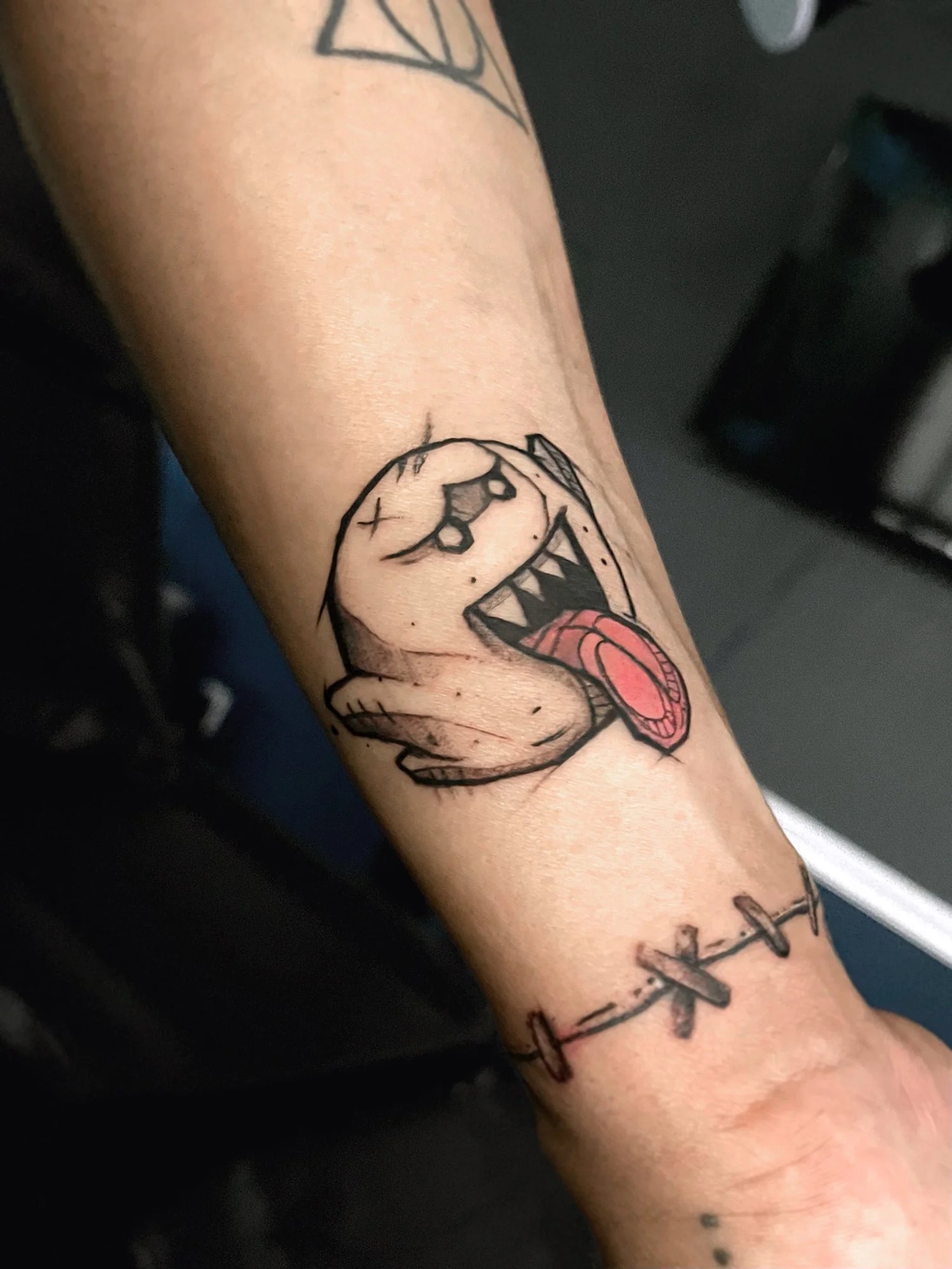 Tattoo of a cartoonish dog with an open mouth and tongue sticking out on the forearm, with barbed wire tattoo around the wrist.