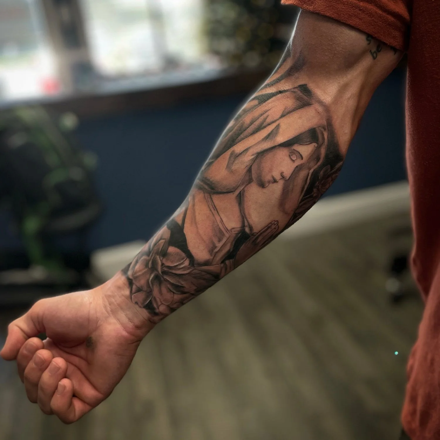 Tattoo of a woman's face on a person's forearm, with hands clasped in a praying position and wearing a head covering