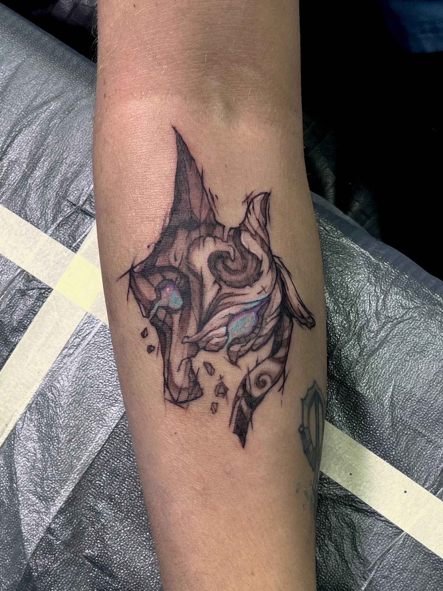 Tattoo of a stylized cat's face with glowing eyes on a person's forearm.
