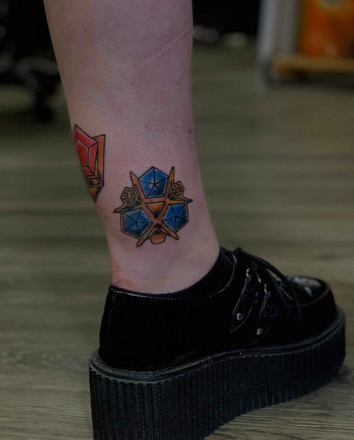 Tattoo of colorful mystical geometric symbols on ankle, with black platform shoe on foot.