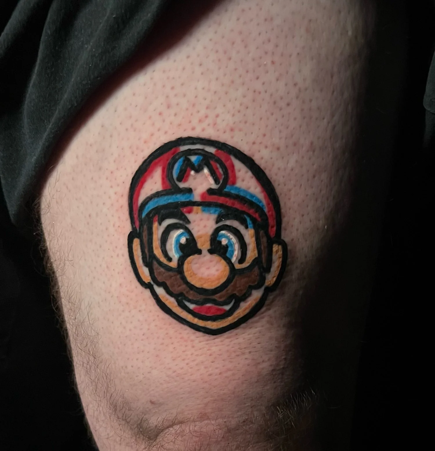 A tattoo of Mario's face from the Super Mario video game series on a person's upper arm.