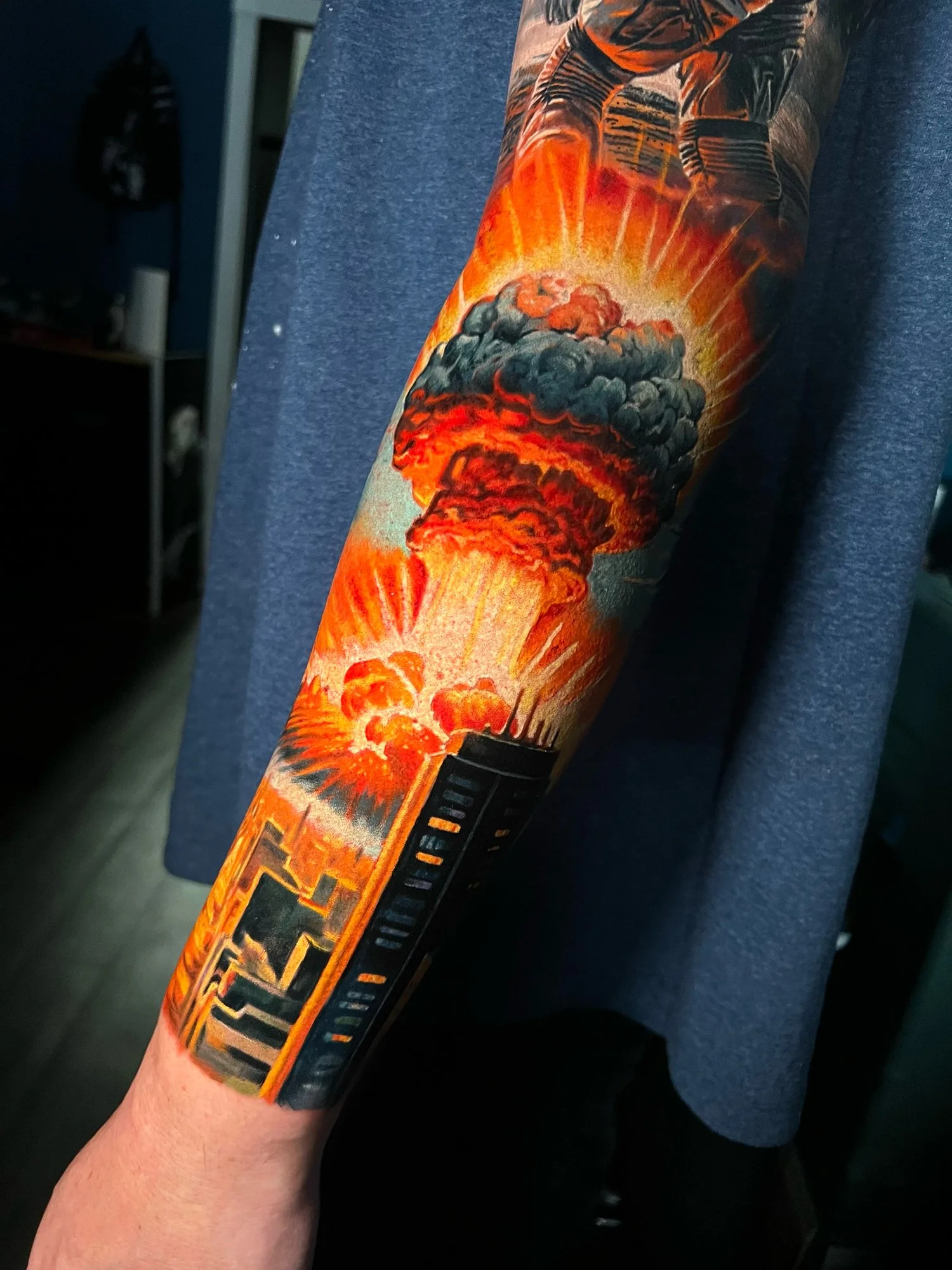 Colorful tattoo of a nuclear explosion with a mushroom cloud, bright orange and black smoke, and the word 'FIESTA' on the forearm.