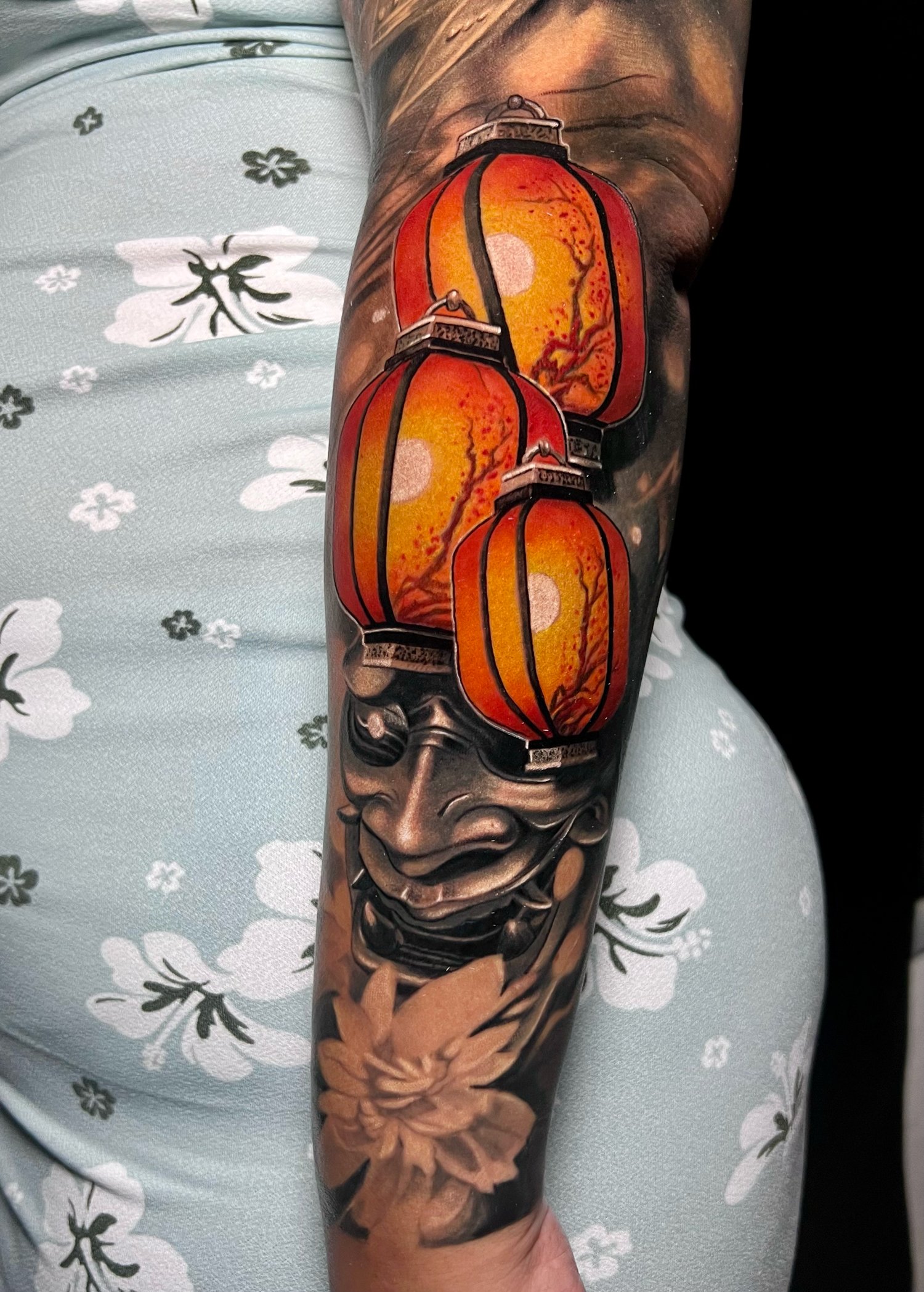 Tattoo of red and orange lanterns and a traditional mask on a person's arm.