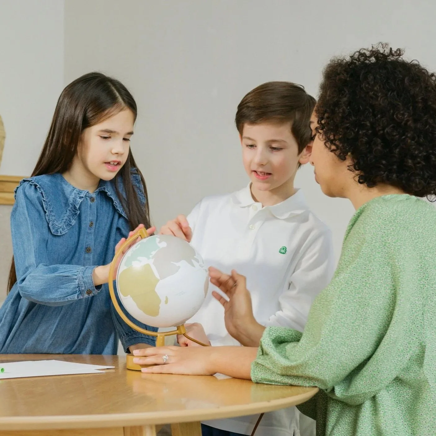 A teacher and two children looking at a globe on a classroom table.