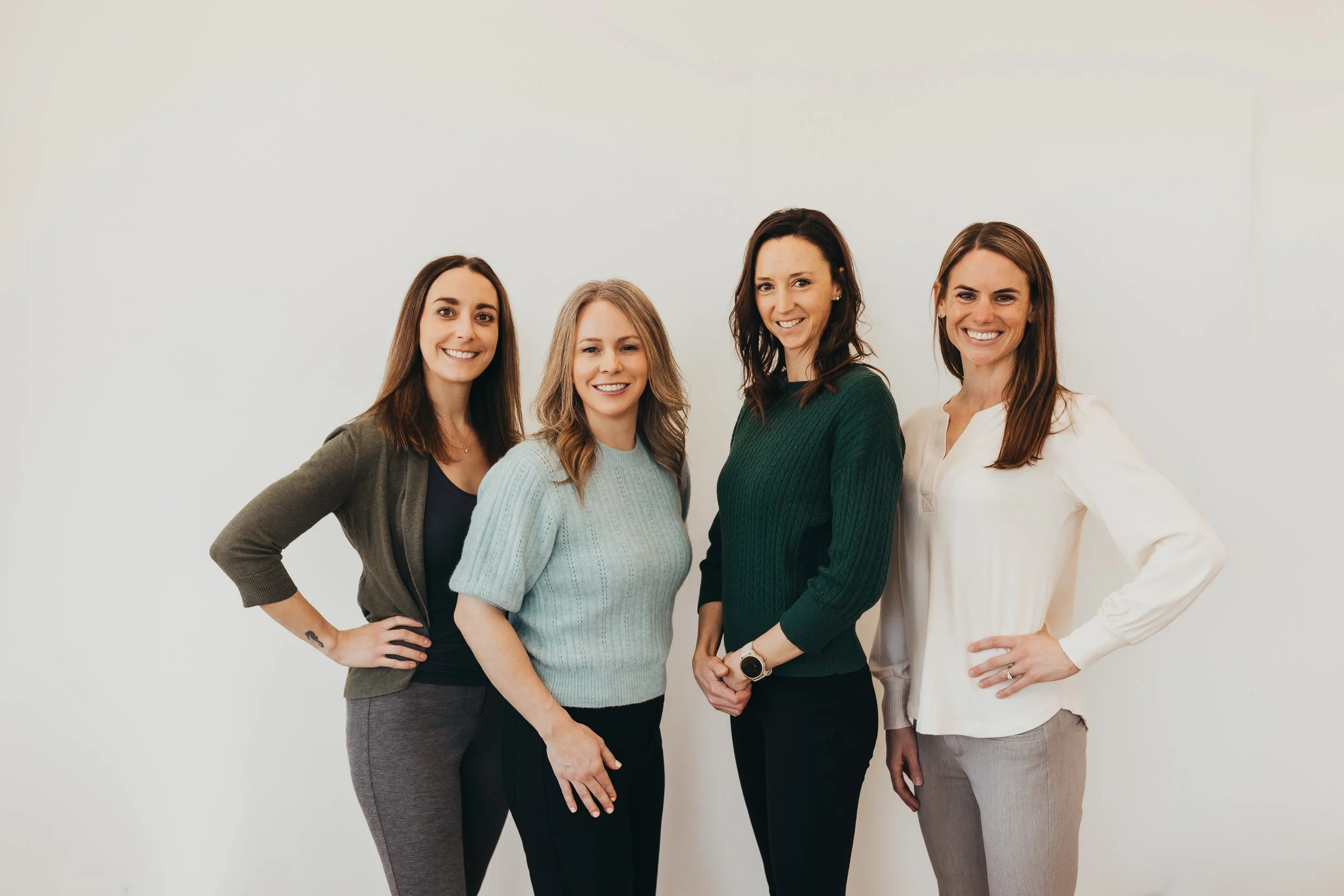 Four women standing together against a white background, smiling at the camera.