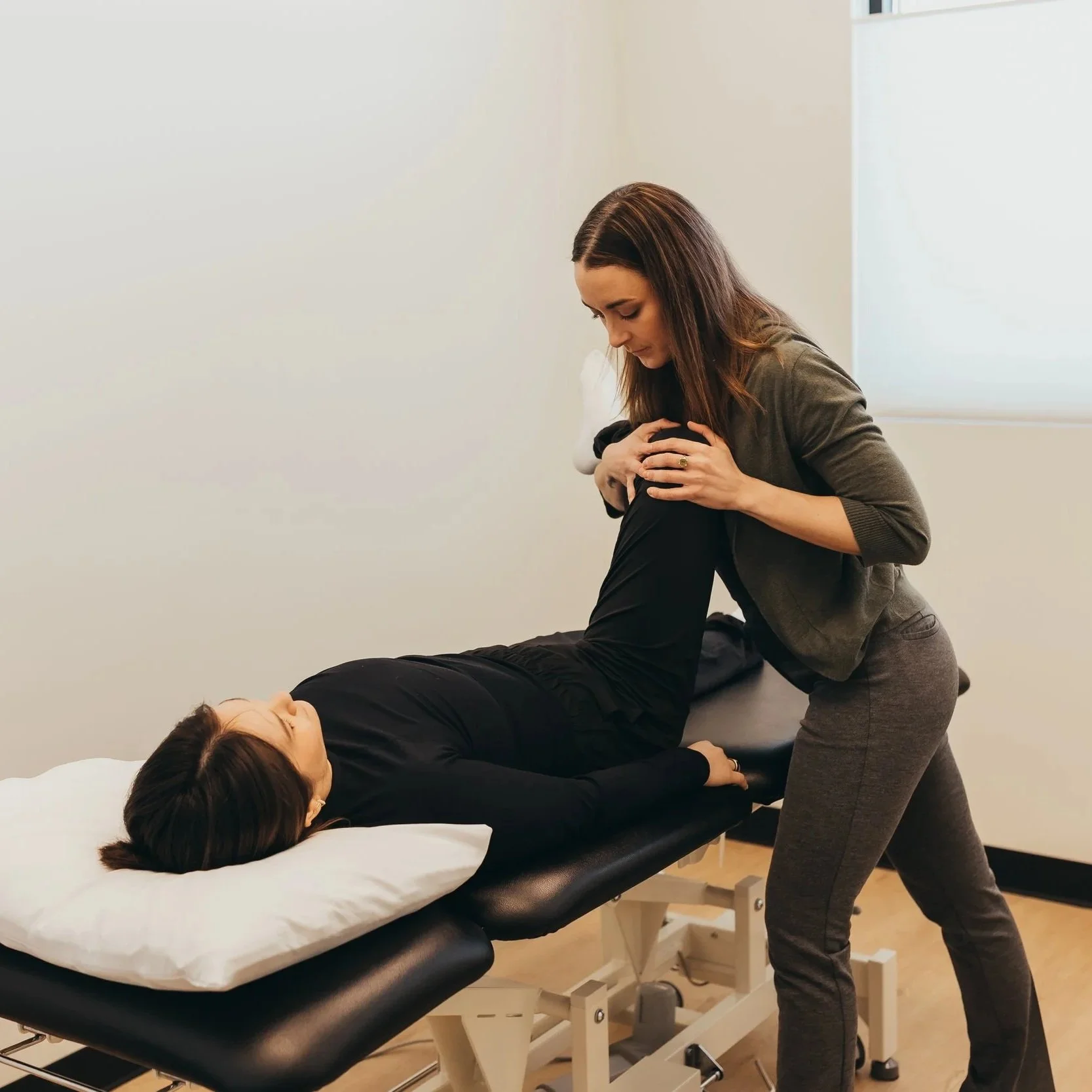 A woman receiving chiropractic care from a female chiropractor in a clinic with white walls and a window.