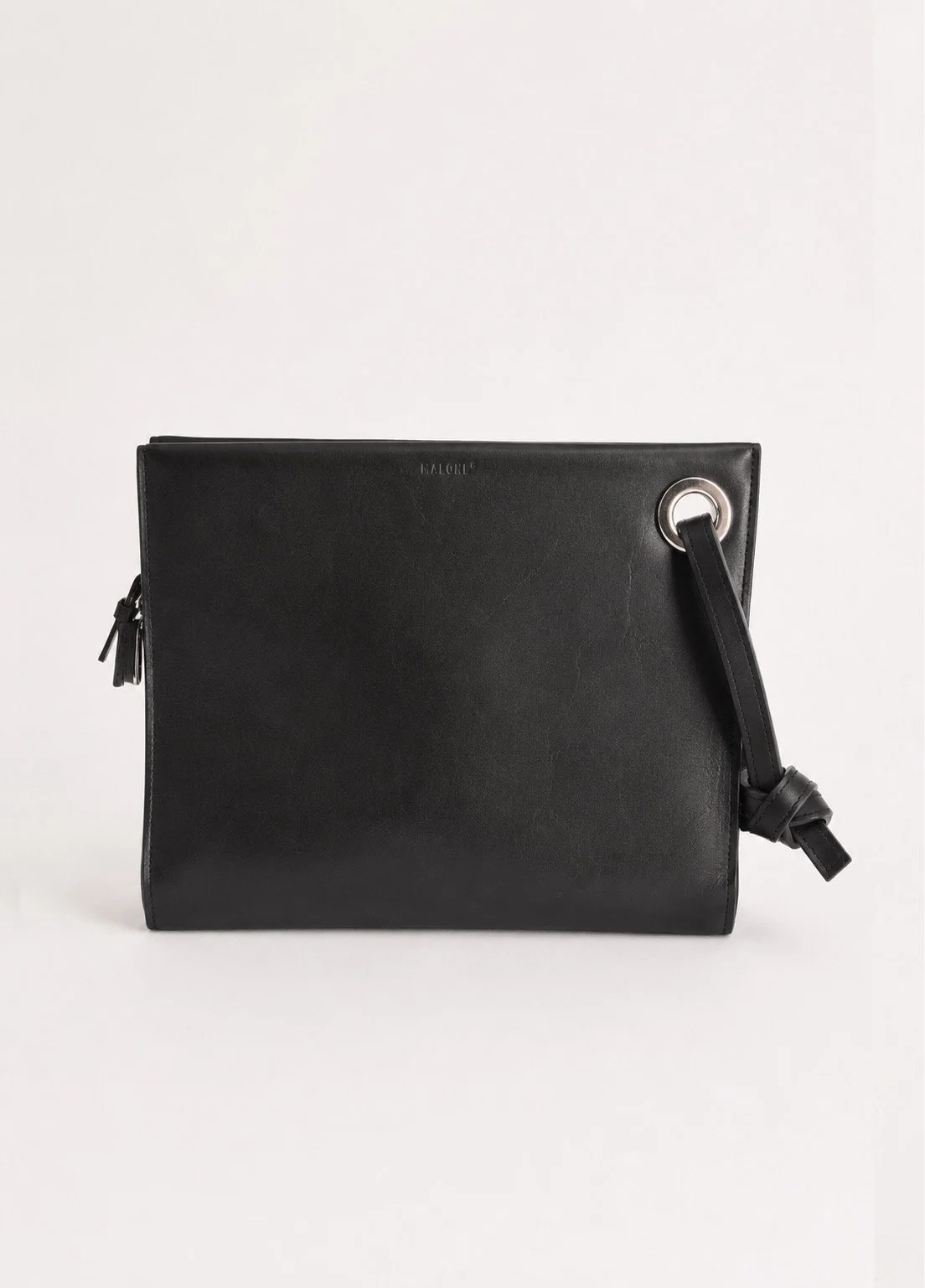 Black leather handbag with a metal ring on the top right corner and a strap tied in a knot.