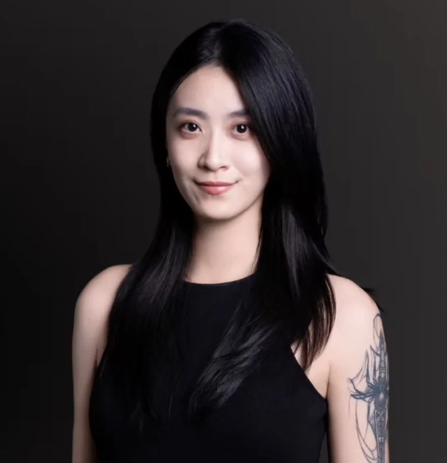 Portrait of a young woman with long black hair, wearing a black sleeveless top, against a dark background.