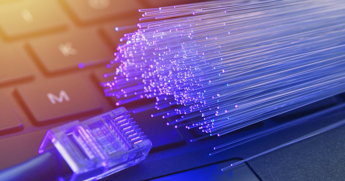 Close-up of a computer keyboard with an Ethernet cable connected, digital fiber optic lines emanating from the connection, symbolizing data transfer.