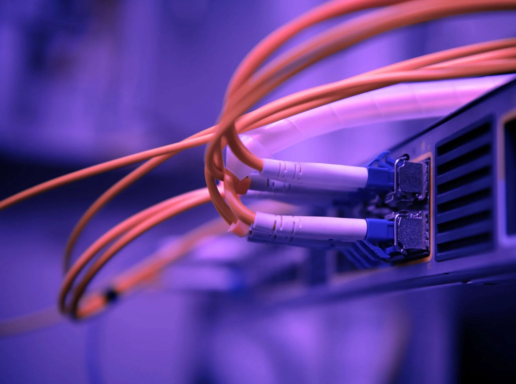 Multiple orange Ethernet cables plugged into a network switch or router with purple lighting.