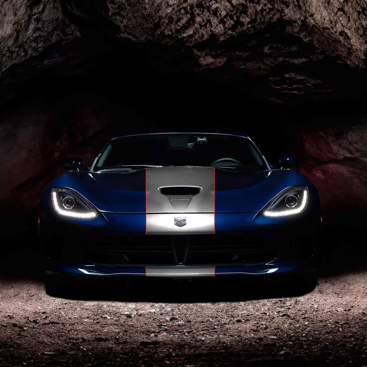 Front view of a blue Dodge Viper with a silver stripe in a dark cave-like environment.