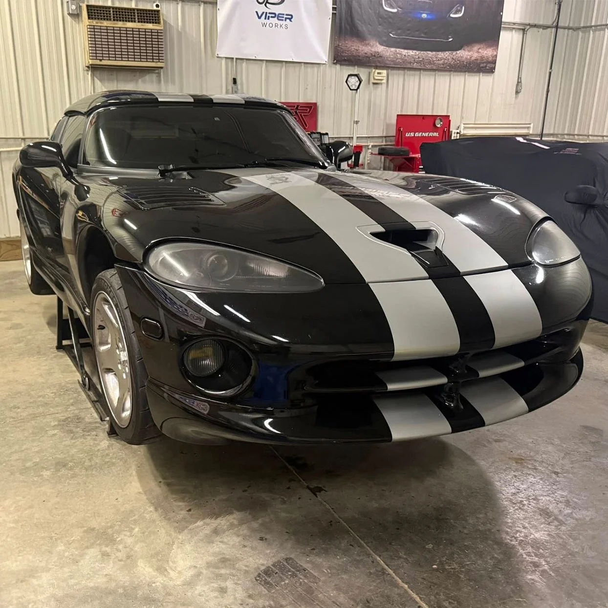 A black Dodge Viper with white racing stripes parked inside a garage.