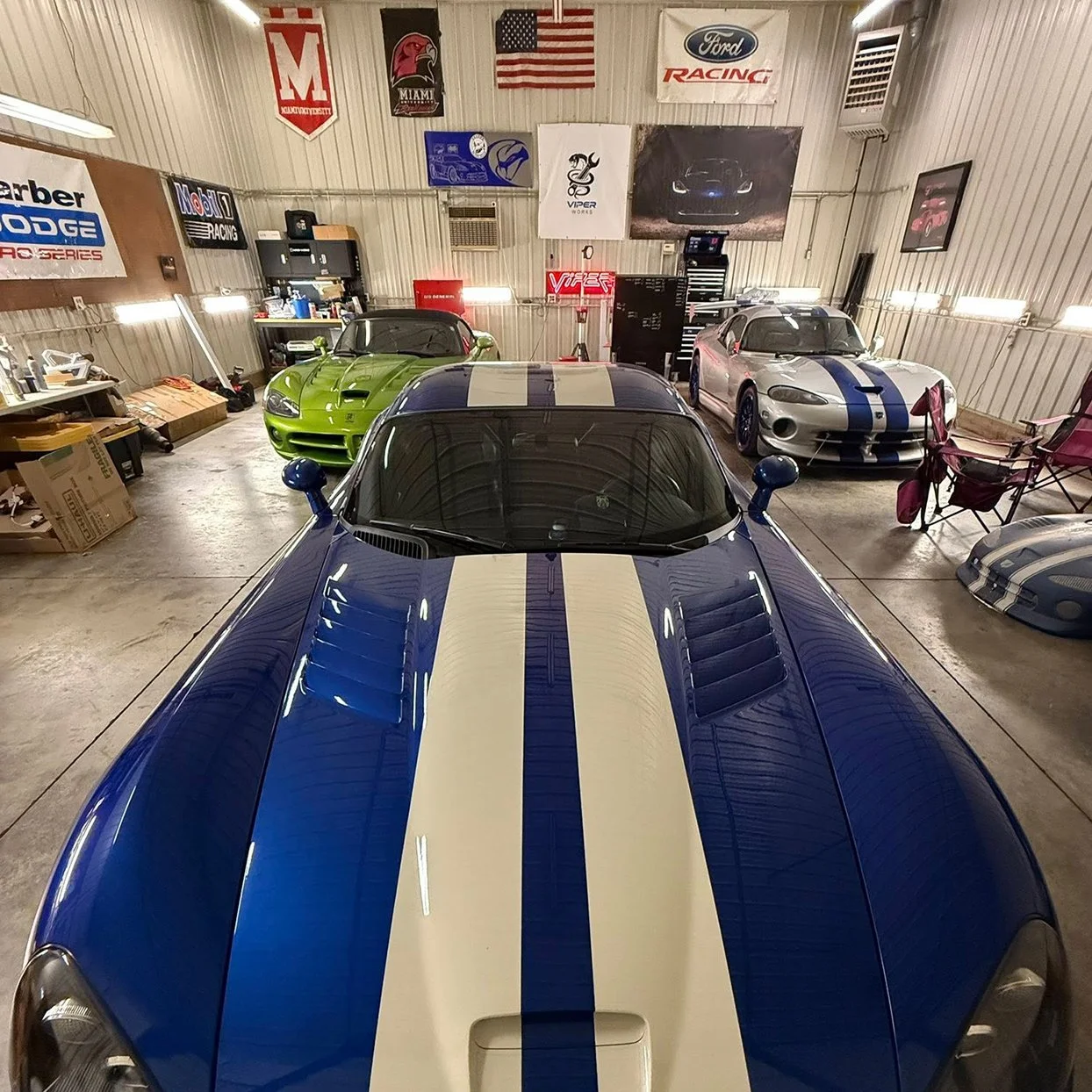 A garage containing three Dodge Vipers with racing stripes, with various automotive posters and signs on the walls.