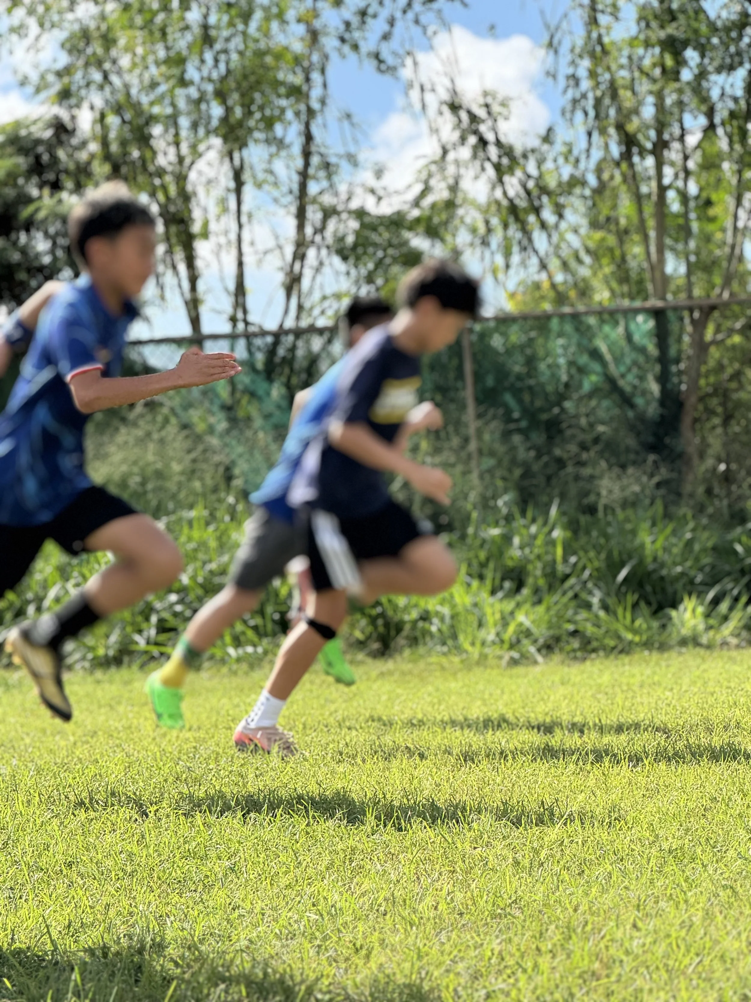 Hawaii soccer players run during their warm up at a private training facility on Oahu with green bushes in the background