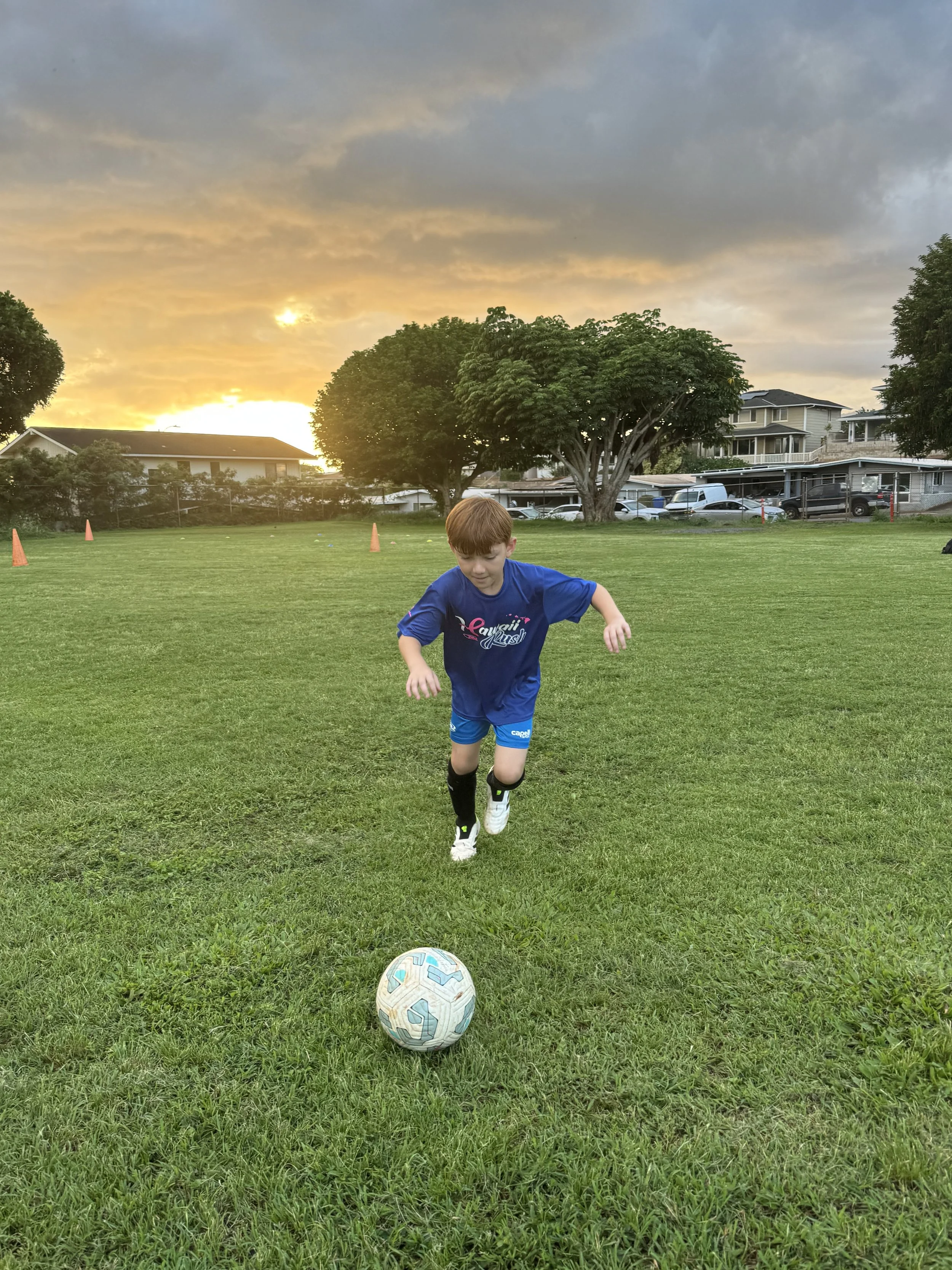 Soccer player runs towards ball to kick it on a field as the sun sets during soccer practice.