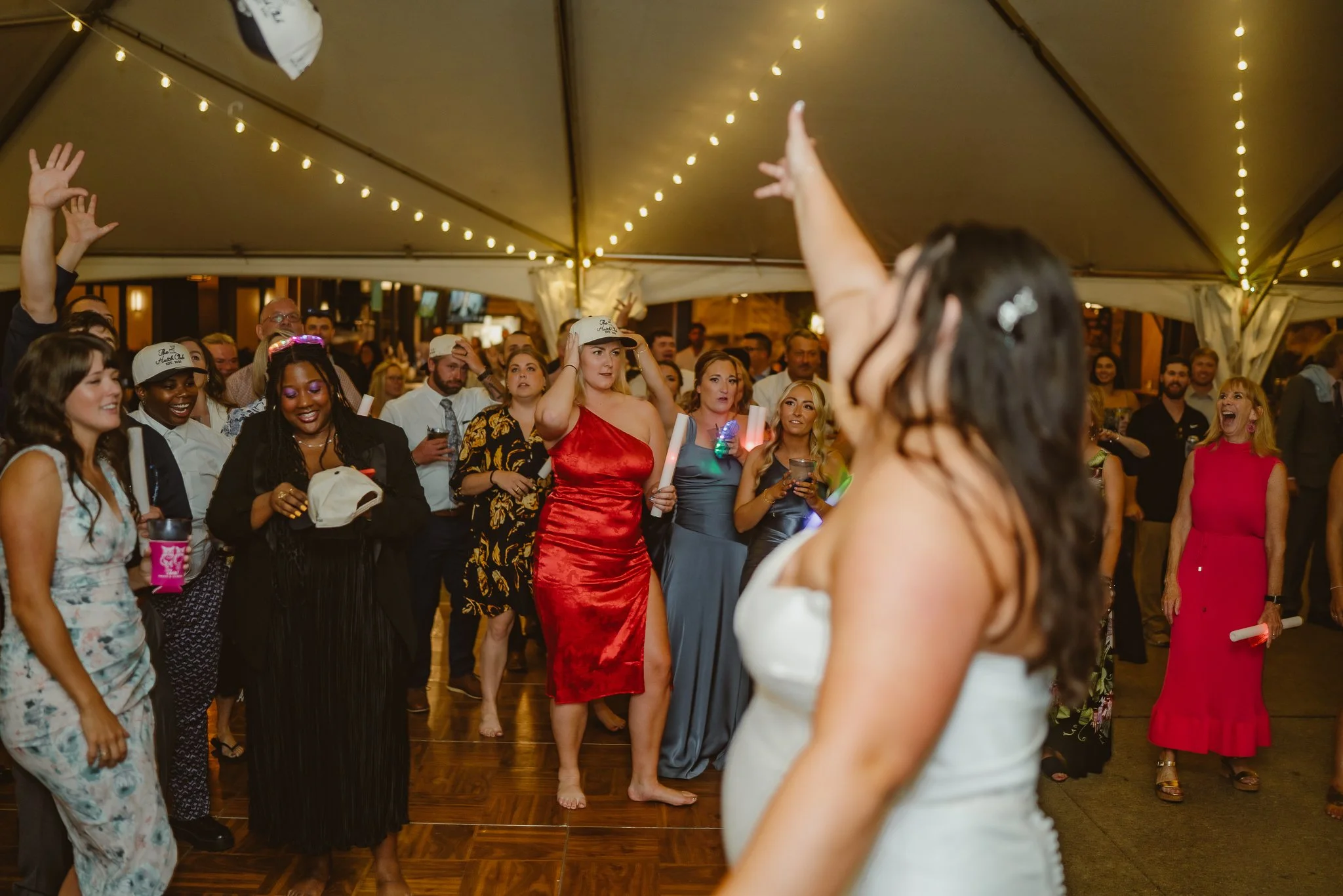 People dancing and having fun at a celebration under a tent with string lights.
