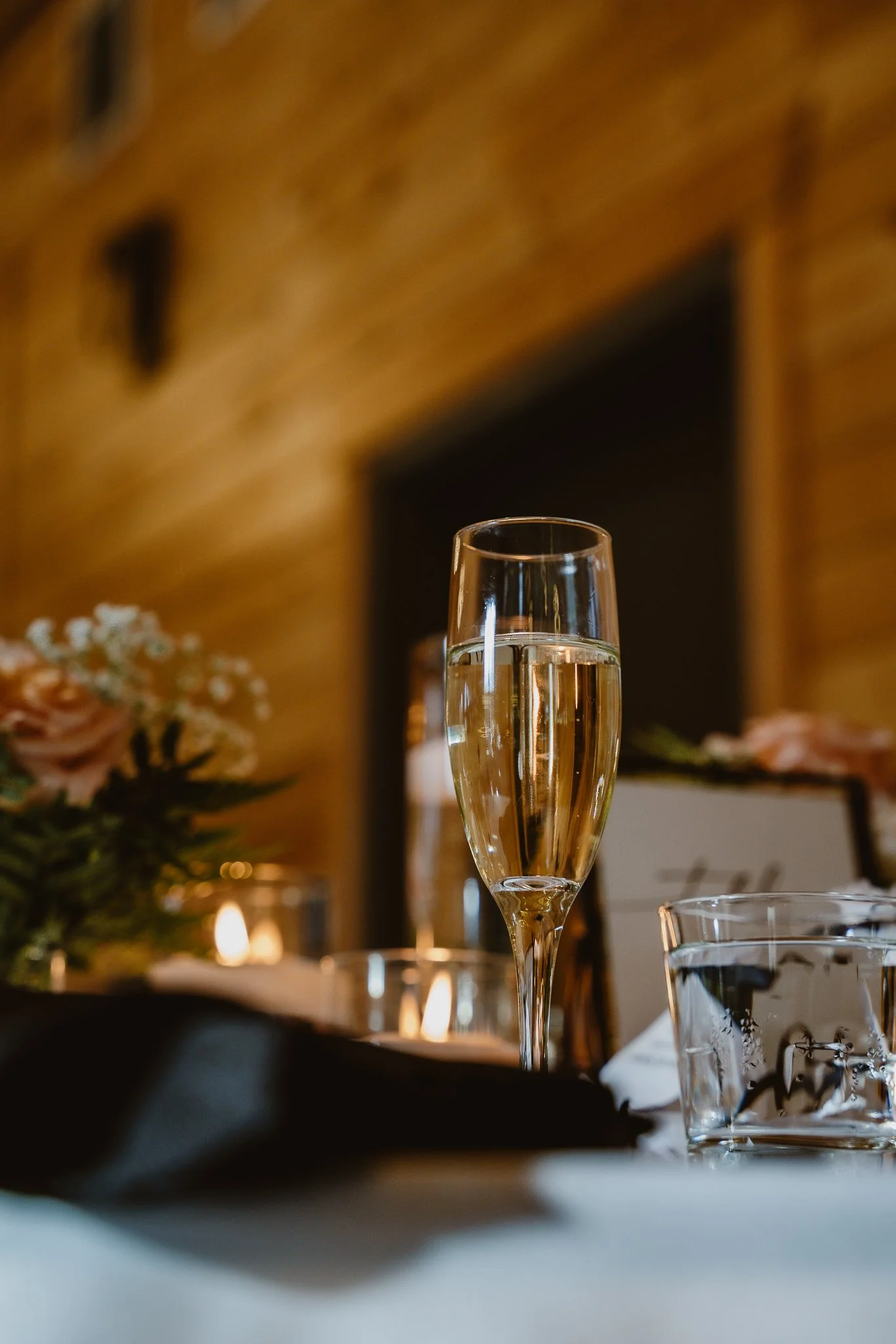 A glass of champagne on a table decorated for a celebration, with flowers and candles in the background.