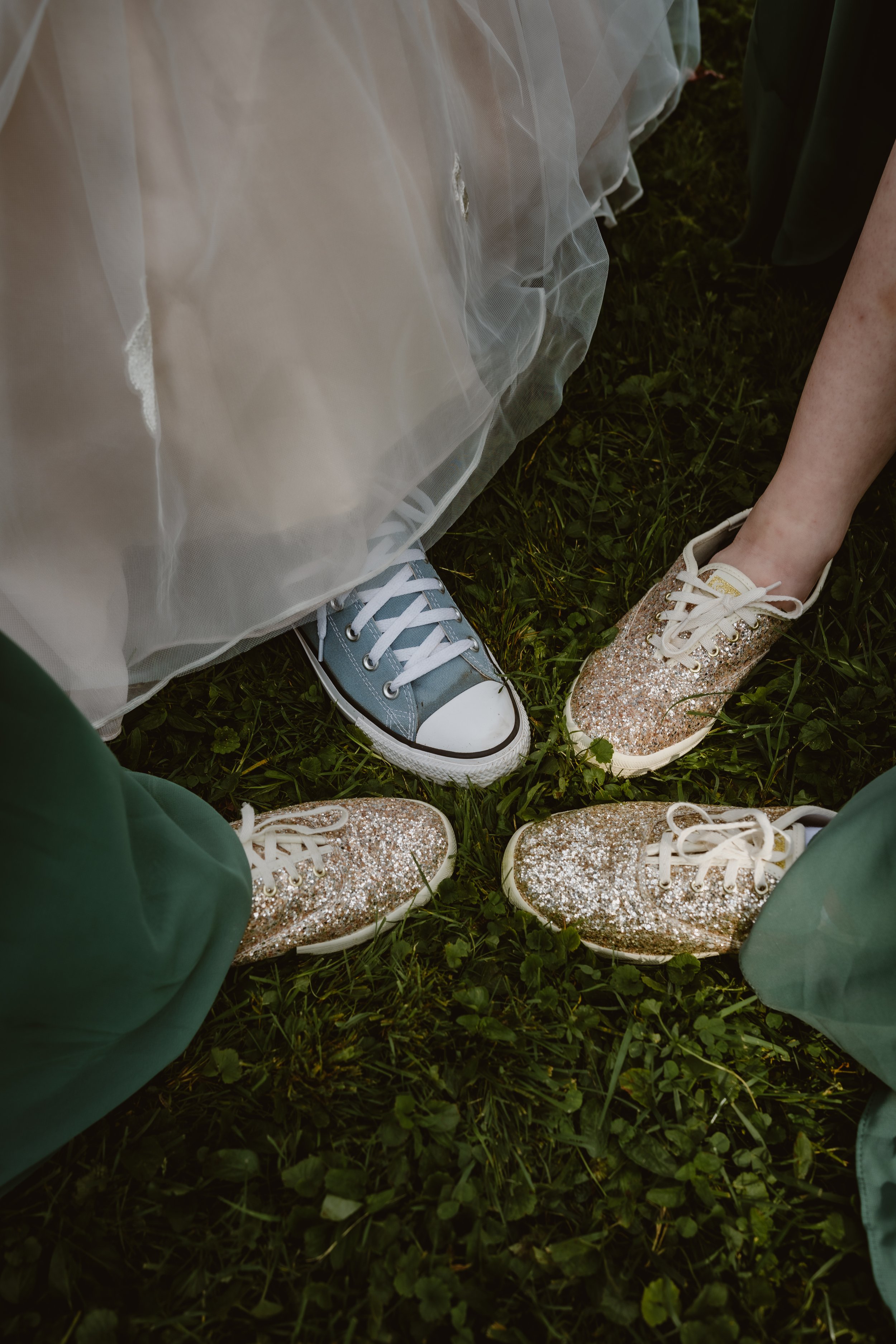 Four people wearing sneakers forming a circle on grass, with two people in glittery shoes, one in a blue sneaker, and one in a beige dress with white shoes. The Grandview of Ellington, Ellington NY
