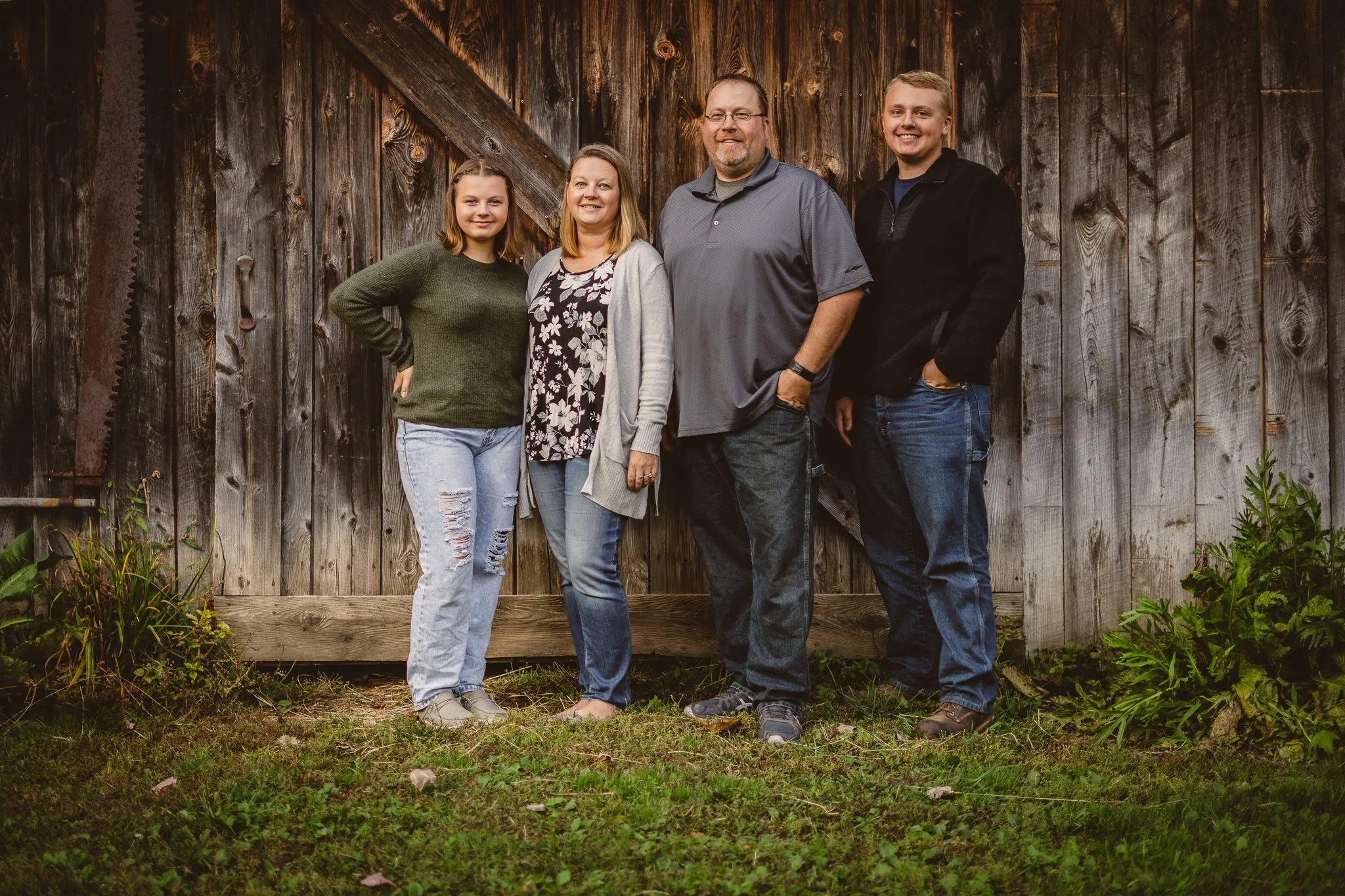 A family of five standing in front of a rustic wooden barn wall, smiling at the camera.