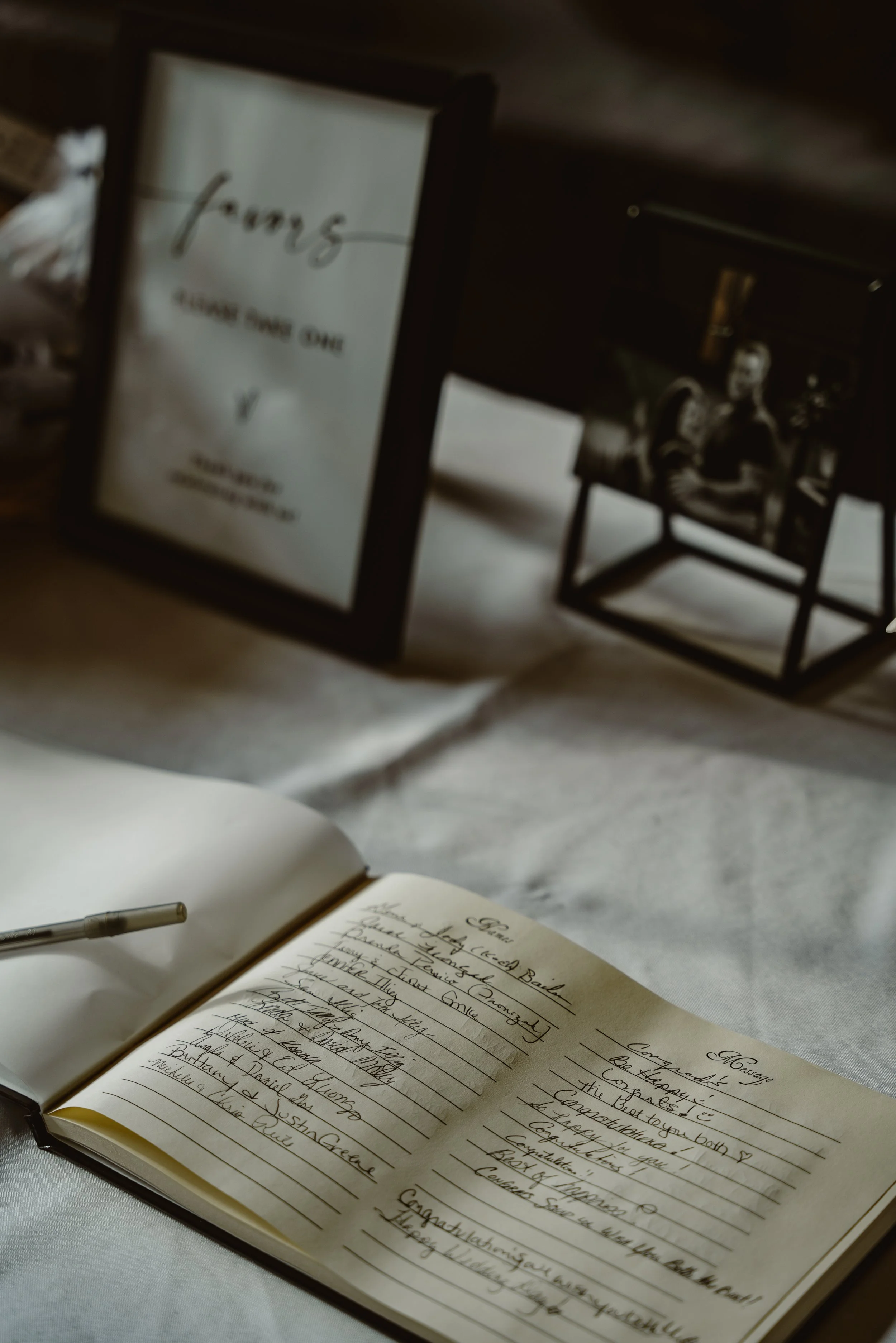 An open notebook with handwritten notes, a pen resting on it, and a framed sign that reads 'fave' and 'HAVE SOME ONE' in the background.