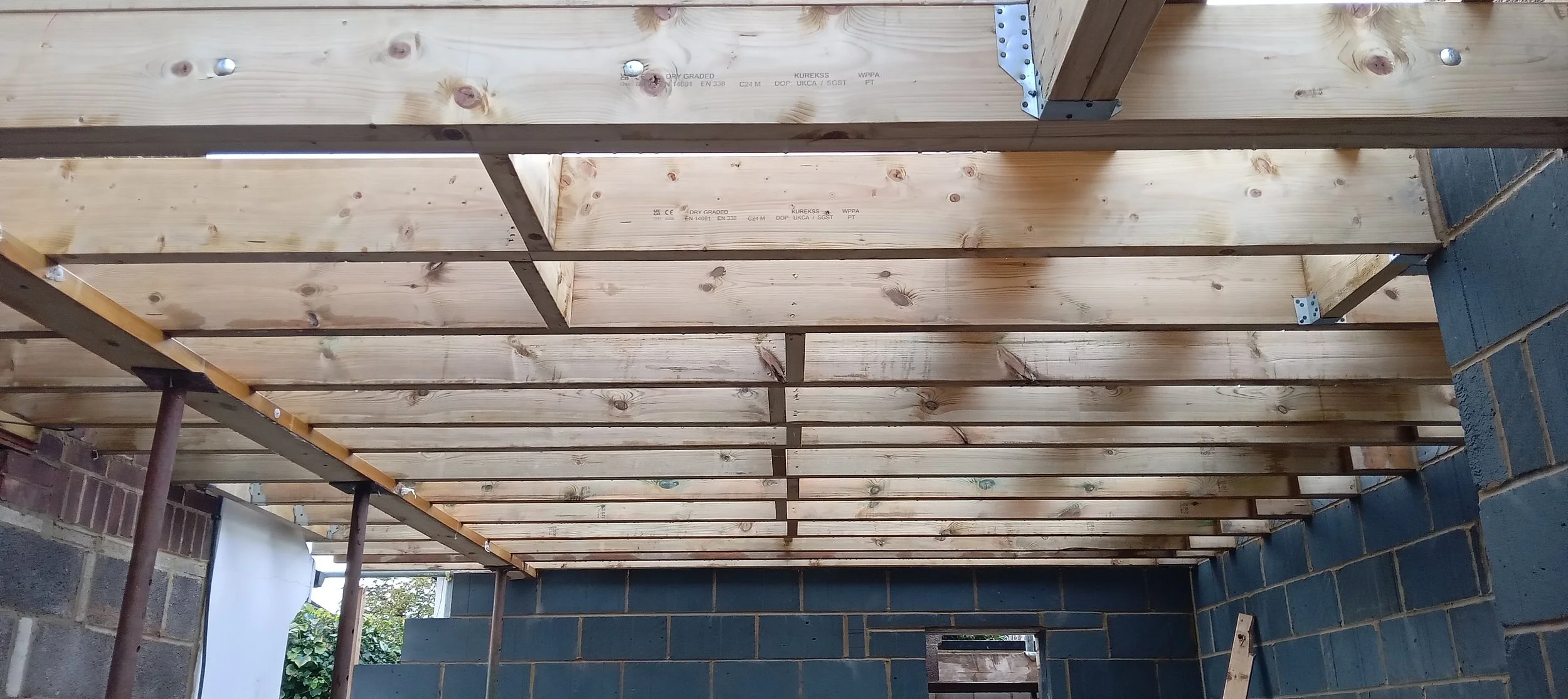 Under construction ceiling with wooden beams and HVAC ducts in a building with partially built brick walls.