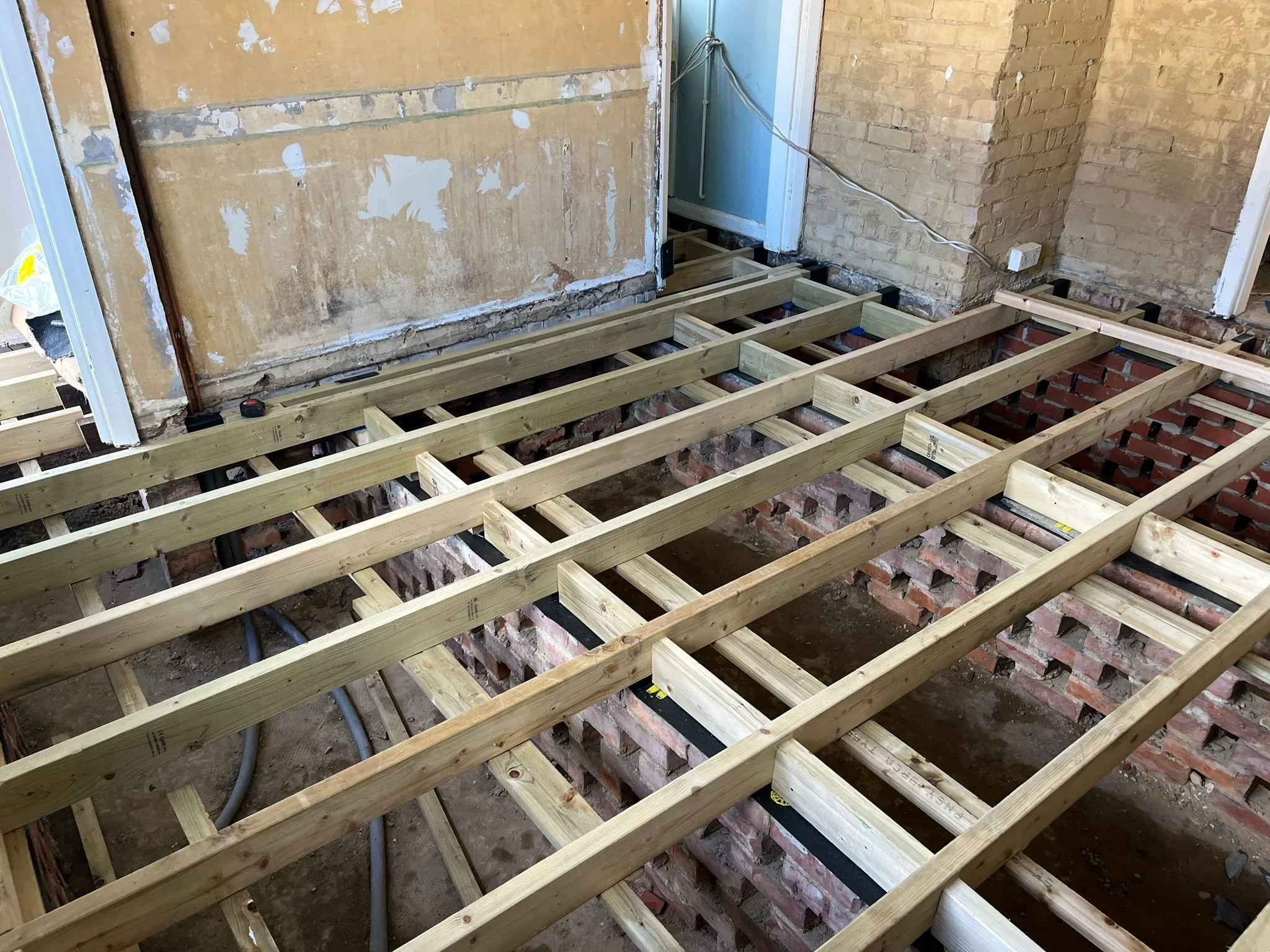 Construction site with wooden floor framework, exposed brick walls, and electrical wiring.