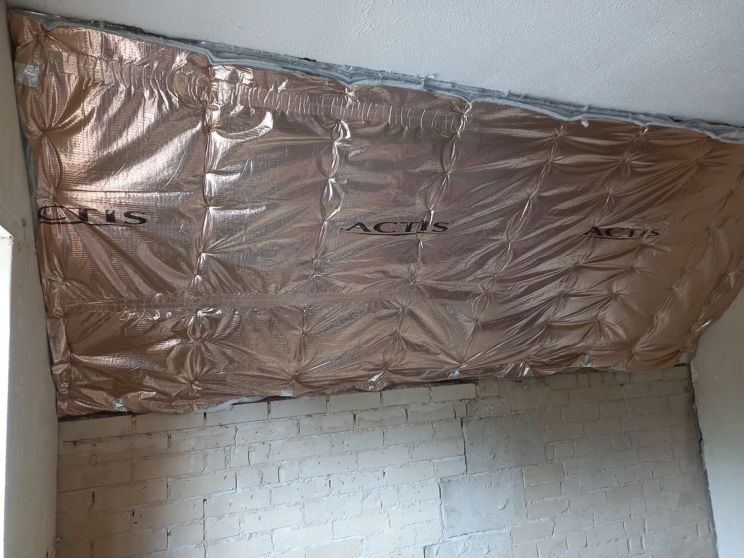 Insulation material labeled 'ACTIS' installed on a wall near a ceiling and brick wall.