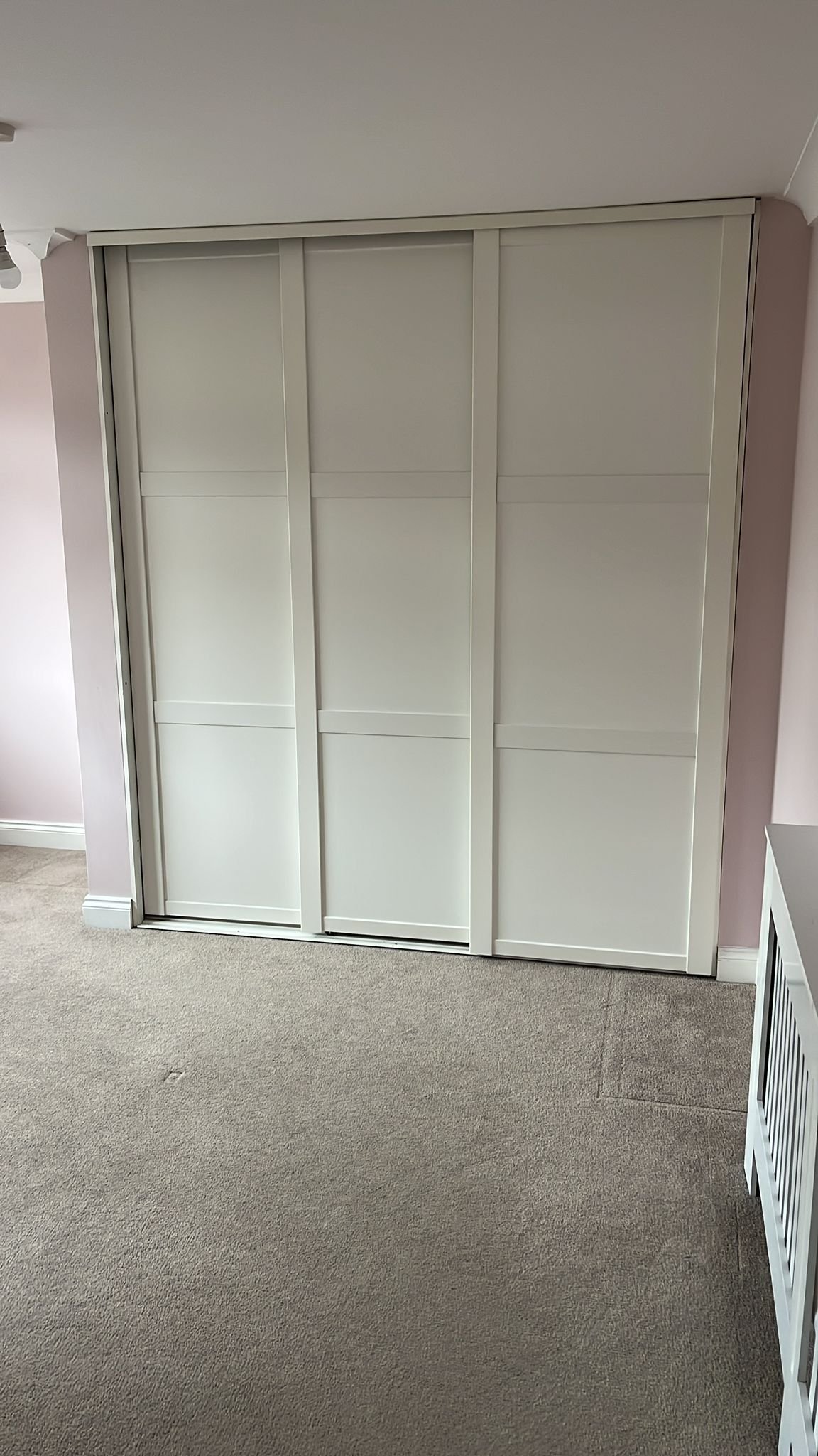White sliding door closet with three panels in a room with beige carpet and light pink walls.