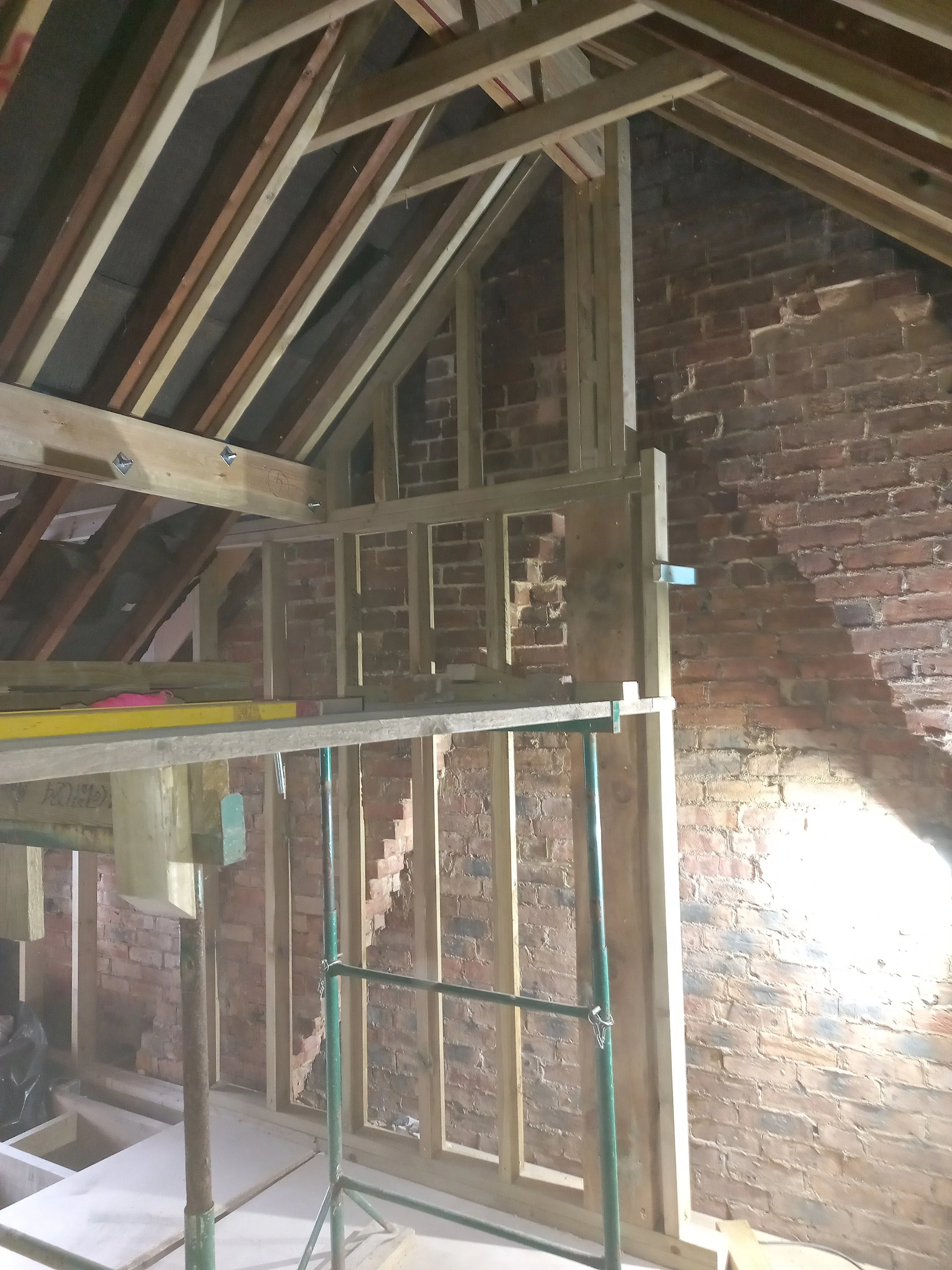 Wood framing and scaffolding inside a building under construction with a brick wall in the background.