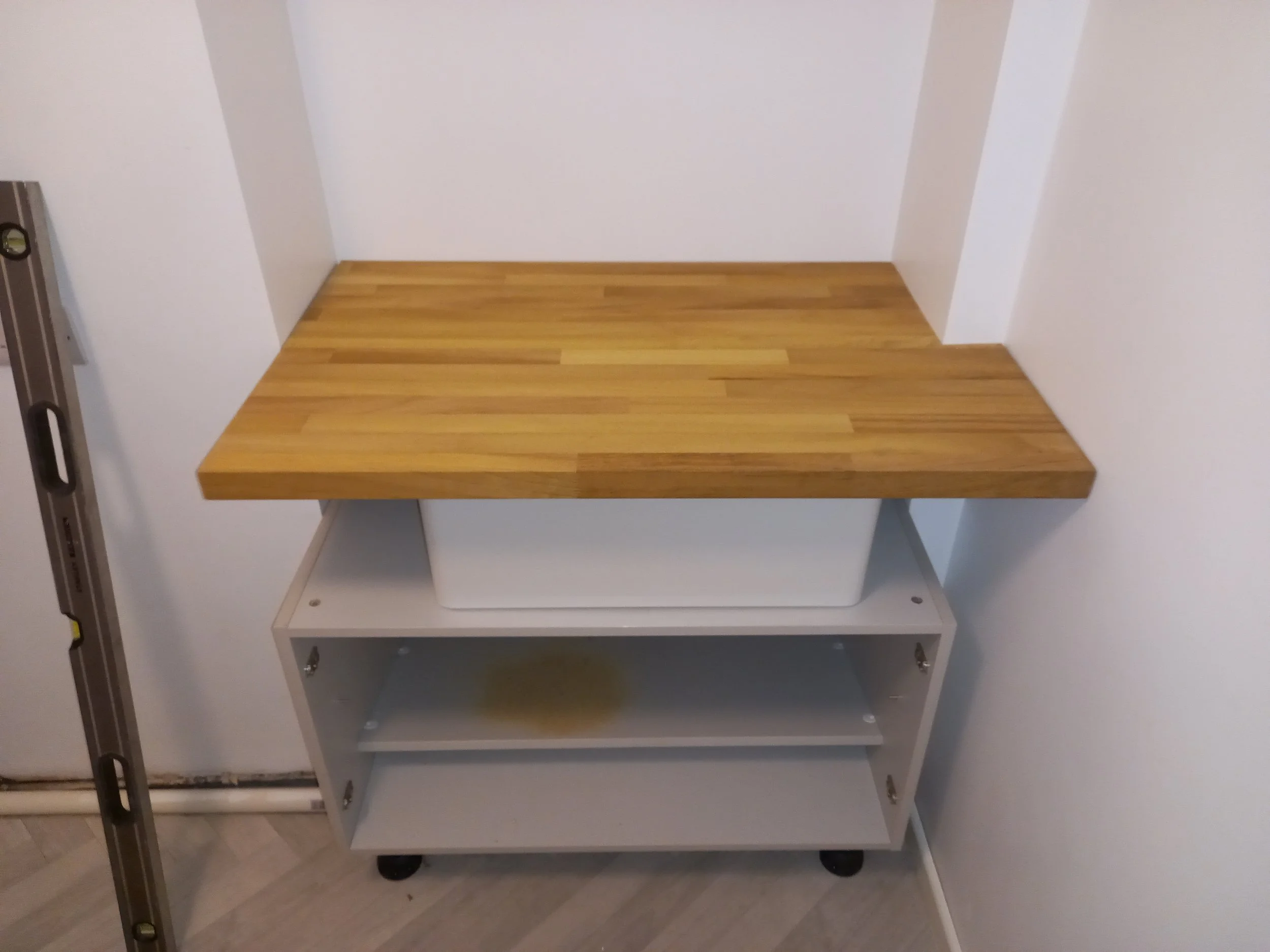Empty white shelving unit with three shelves, positioned in front of a wall, dark flooring, and located near a door or opening on the left side of the image.