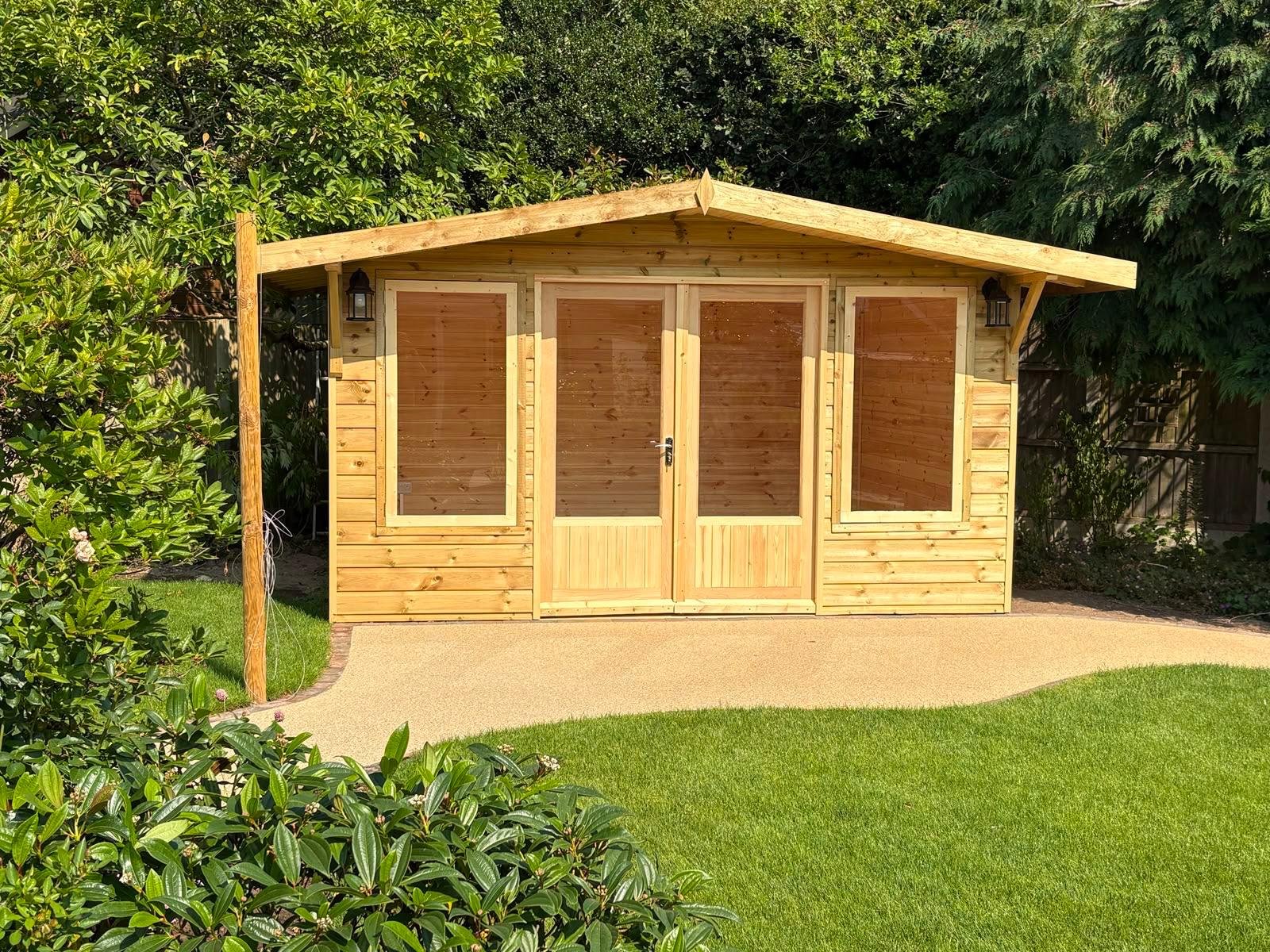 A newly built wooden garden shed with double doors and large windows, situated on a landscaped lawn with trimmed grass, surrounded by lush greenery and bushes.