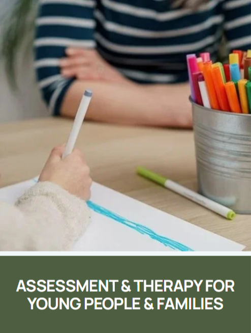 Children's Therapy or psychology session with a child. Child holding a blue colored marker, drawing on paper, with a container filled with colorful markers on the table.  A therapist in a striped top sits nearby. Child assessment or therapy session.