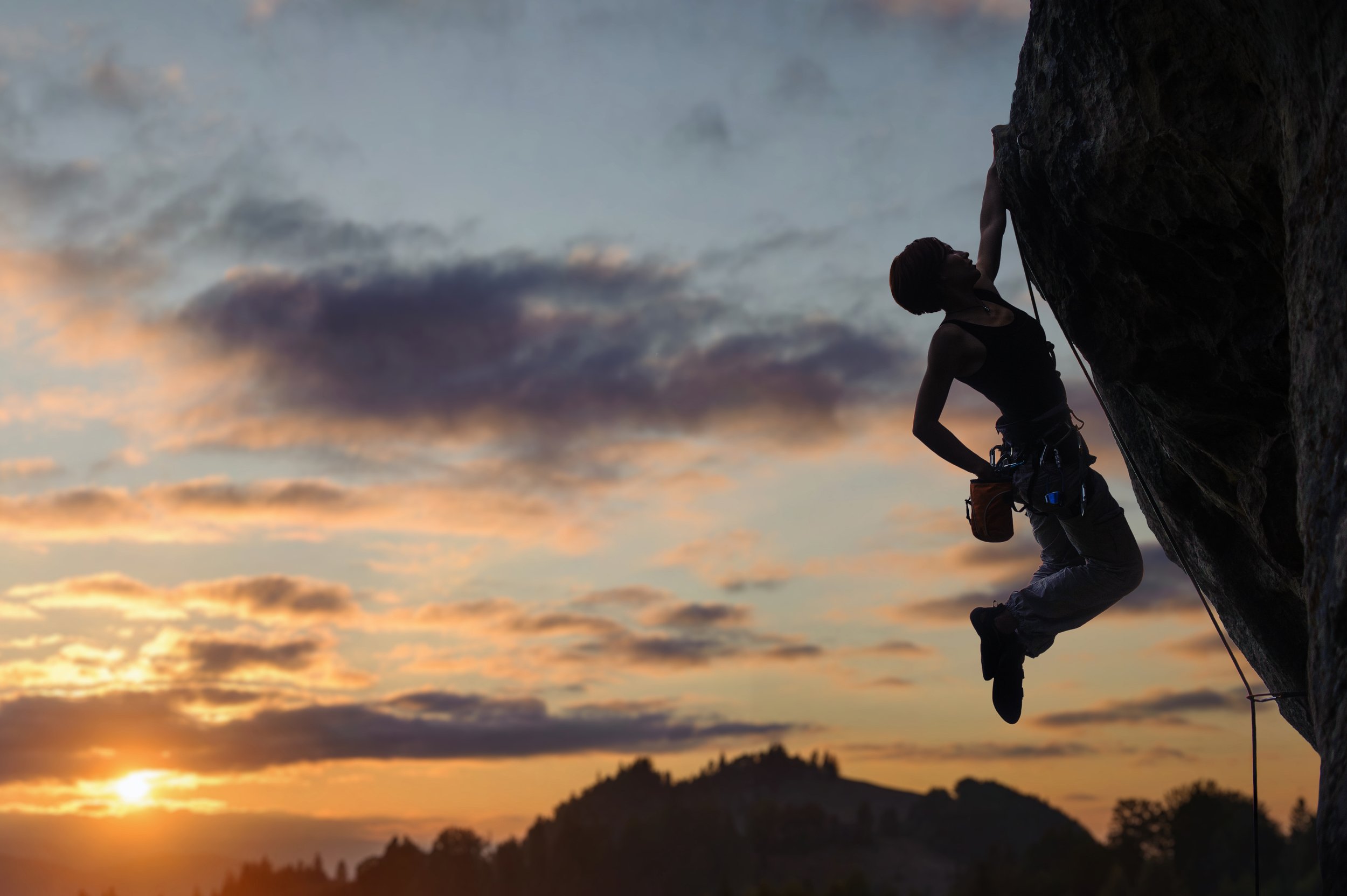 Silhouette of a person climbing a rock face during sunset.