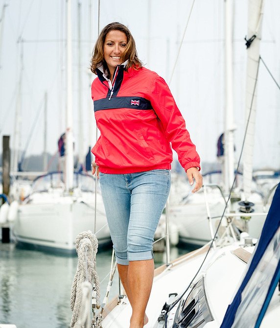 Woman smiling on a sailboat at a marina, wearing a red jacket and jeans.