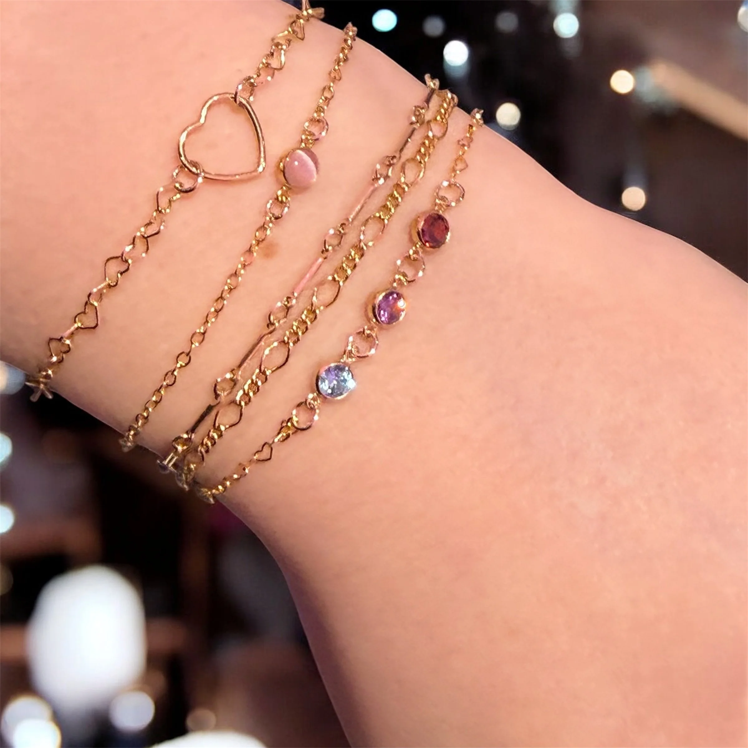 Multiple gold filled welded bracelets with heart and birthstones charms on a person's wrist.