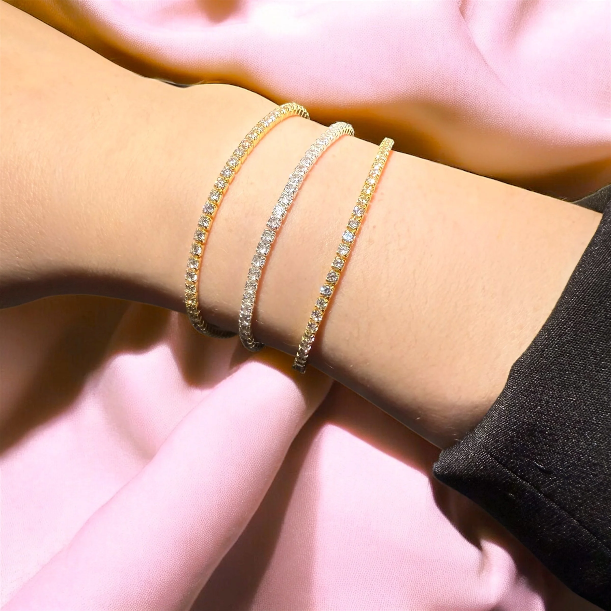 Three elegant permanent welded tennis bracelets on a woman's wrist, with satin pink and black fabric as background.