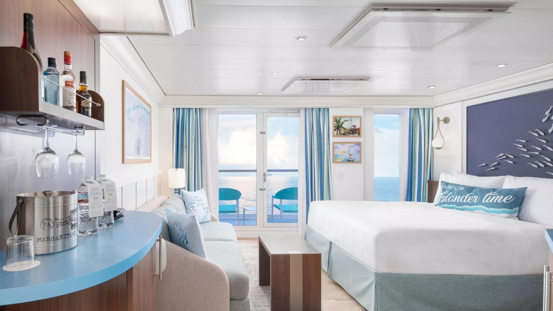Interior of a cruise ship room with a large bed, ocean view balcony, blue curtains, and seaside decor.