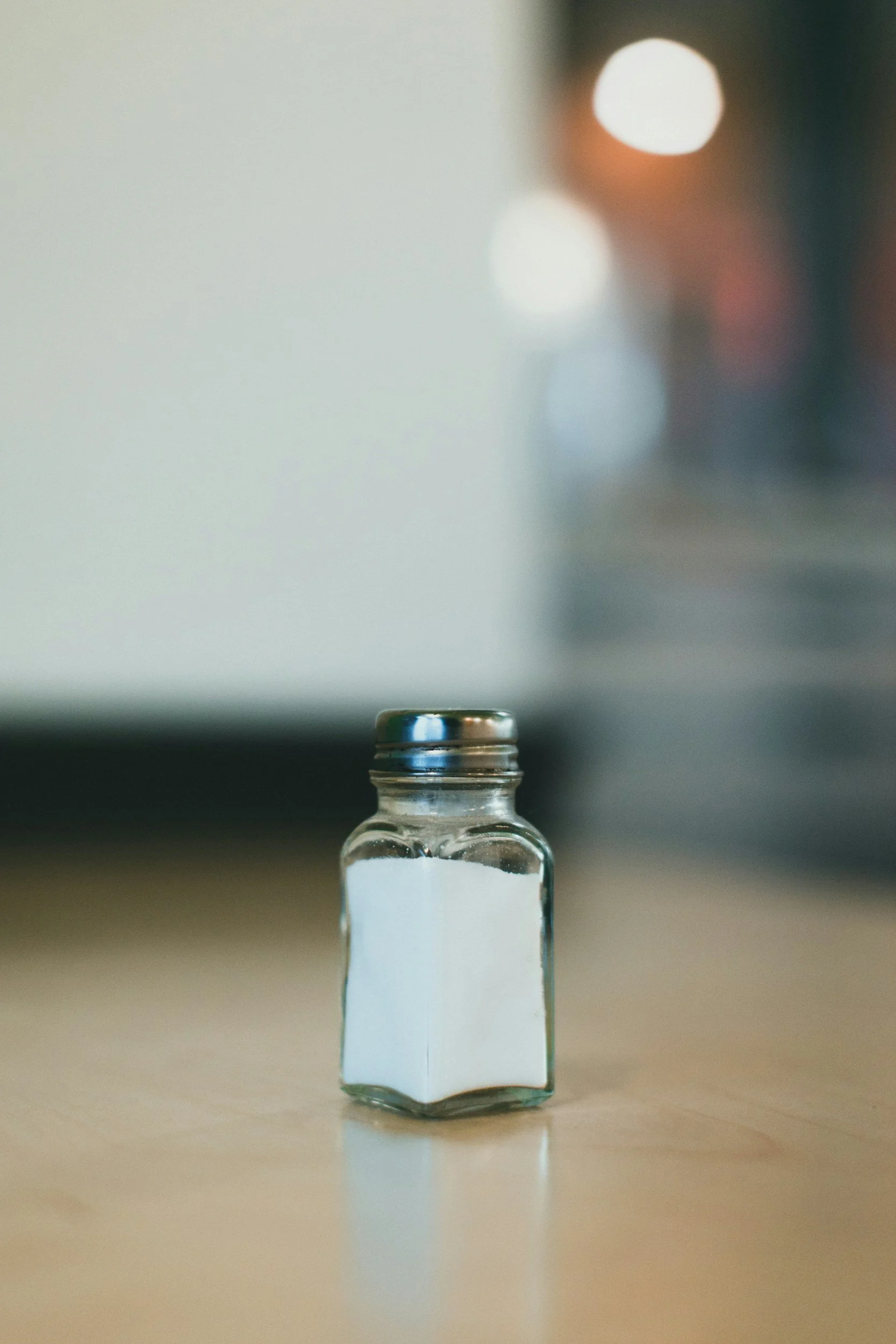 Small glass salt shaker on a wooden surface with a blurred background.