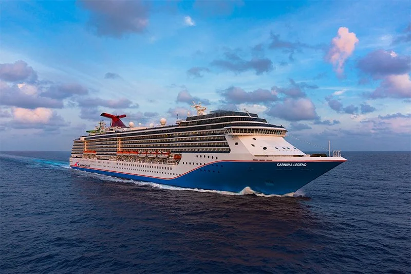 A large cruise ship named Carnival Legend sailing on the ocean under a partly cloudy sky.