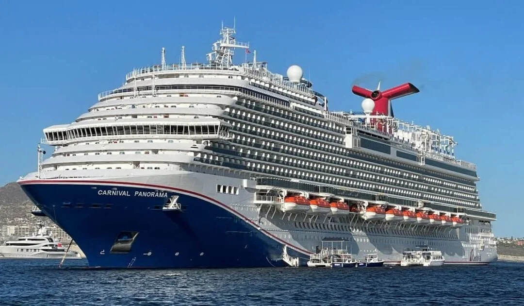 A large cruise ship named Carnival Panorama docked at the port, with multiple decks, white and blue exterior, and red funnel, against a clear blue sky.