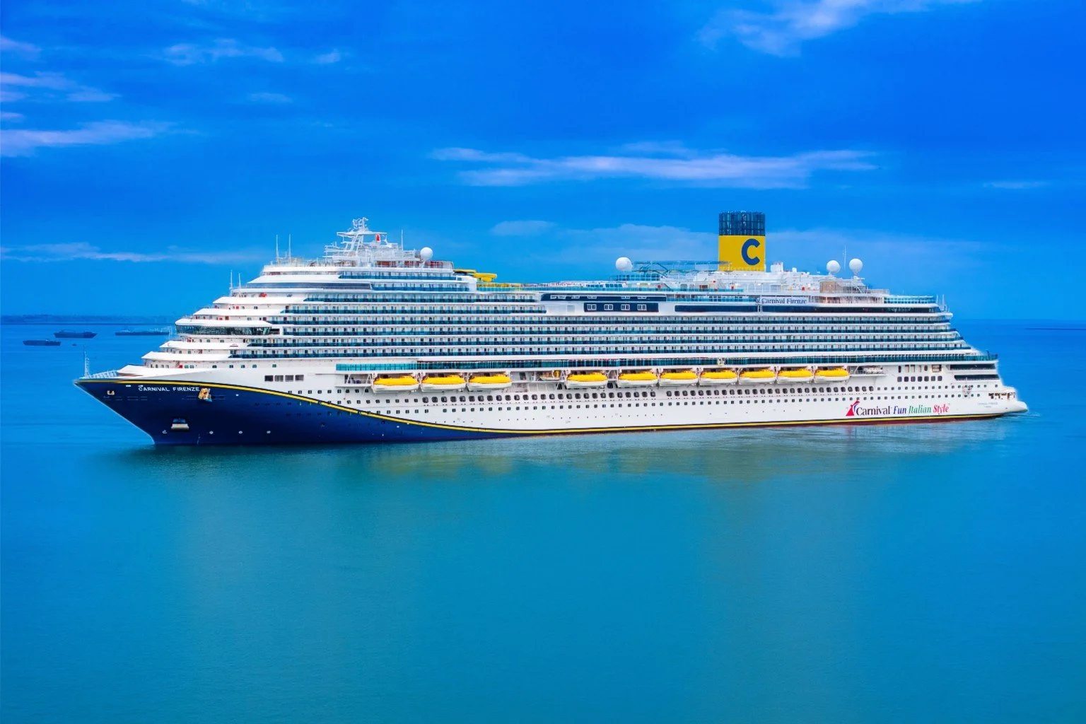 A large cruise ship sailing on calm blue ocean waters with a mostly cloudy sky in the background.