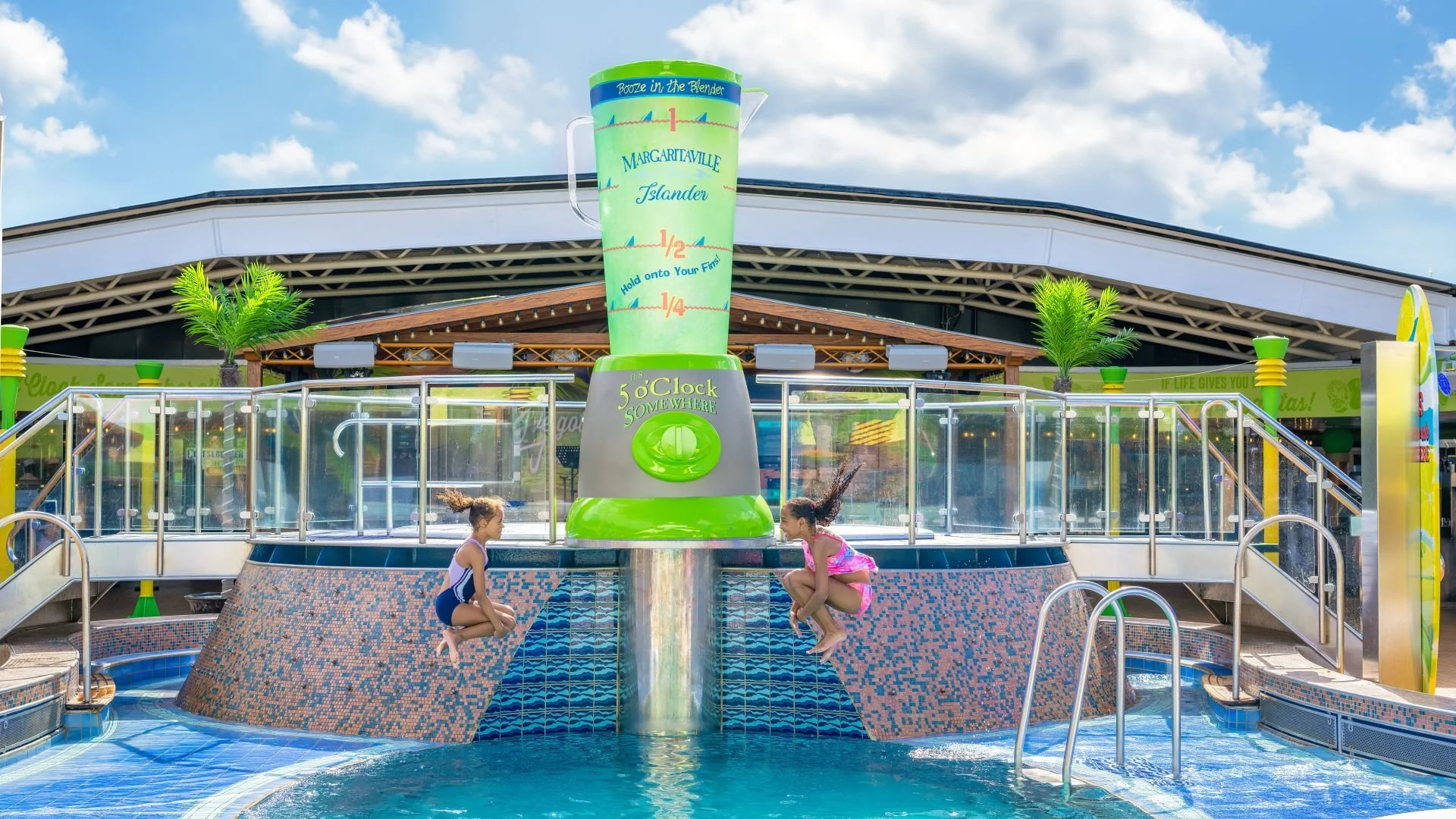 Two children jumping into a pool at an outdoor water park with a large measuring fountain feature in the background, under a partly cloudy blue sky.