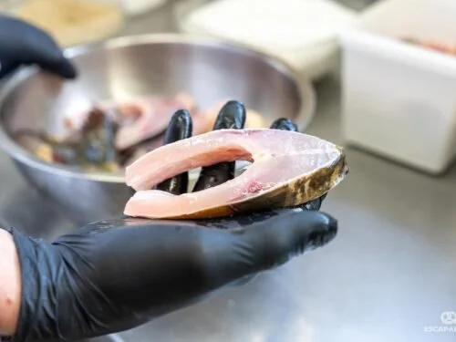 Une main gantée tient un filet de poisson cru dans une cuisine 