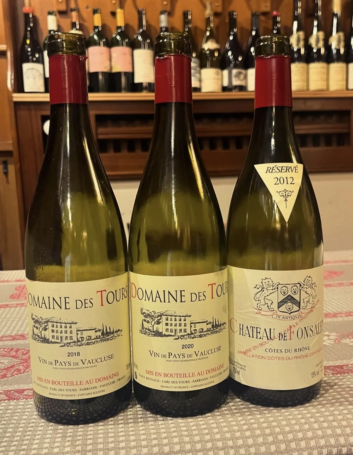 Trois bouteilles de vin blanc avec des étiquettes indiquant Domaine des Tours, année 2018, 2020, et Château de Fonsalette, réserve 2012, sur une table.
