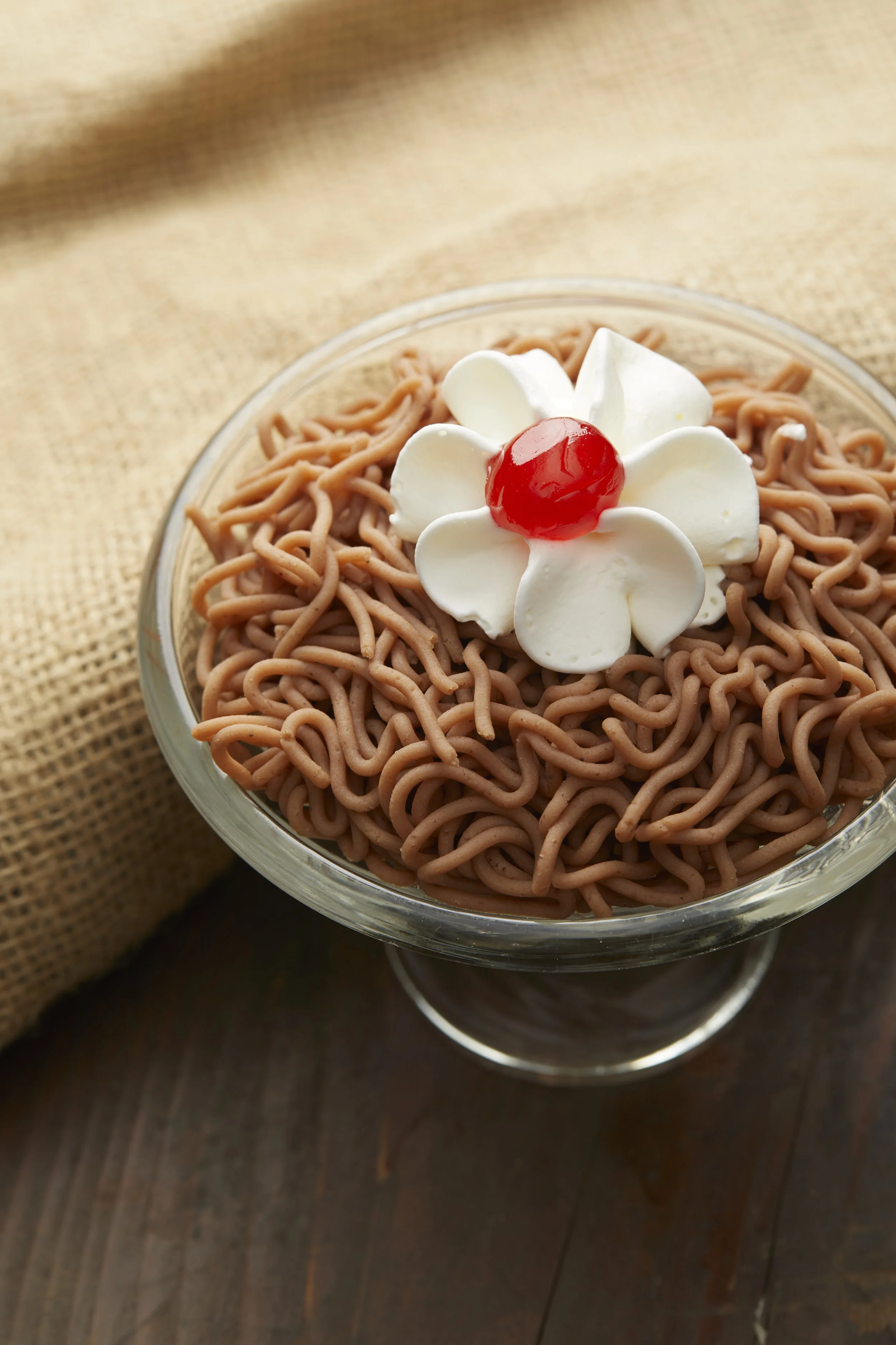 Torche aux marrons, Dessert dans un bol transparent, décoré d'une fleur en crème et d'une cerise confite rouge.