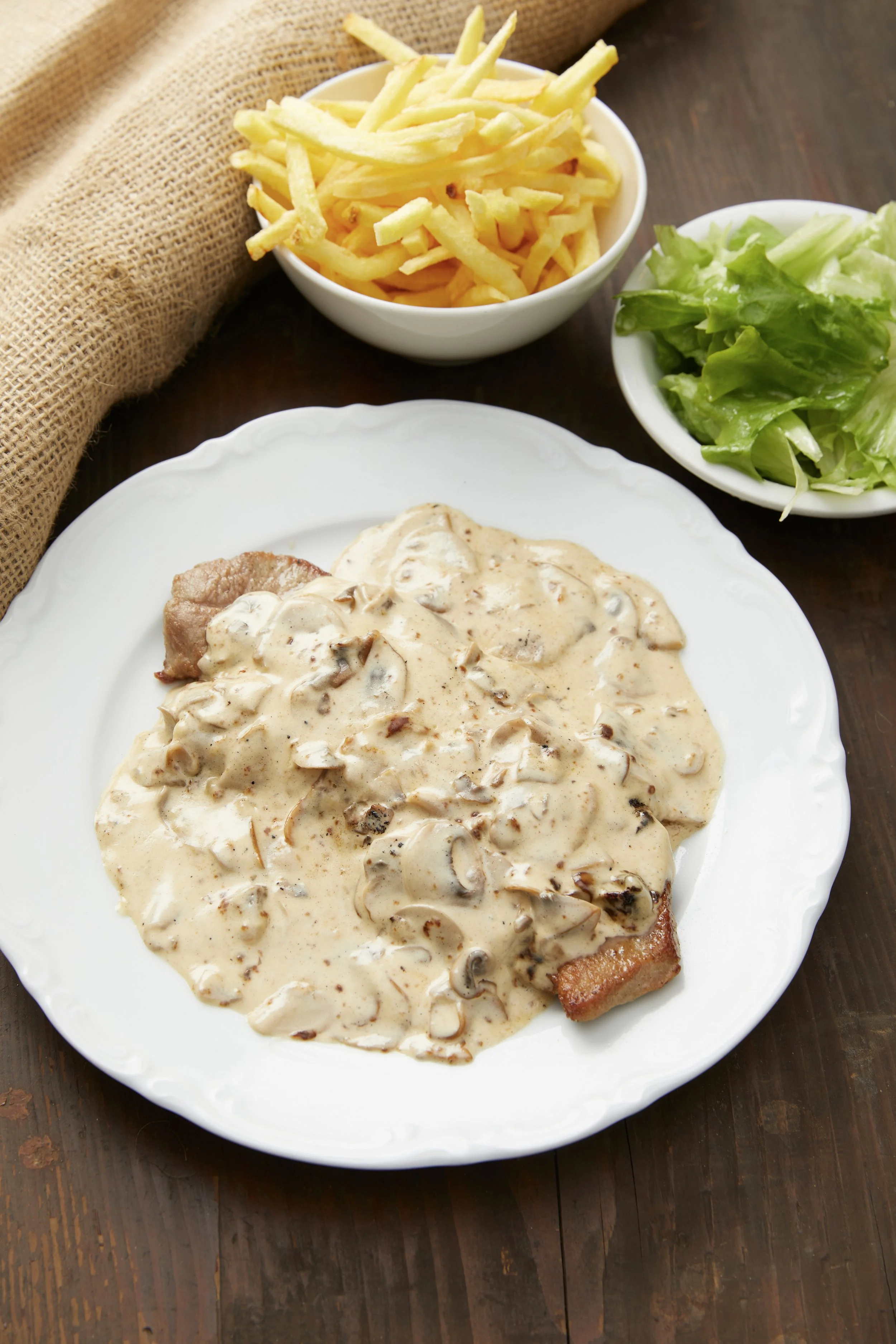 Une viande avec une sauce aux champignons, accompagné de frites et de salade verte
