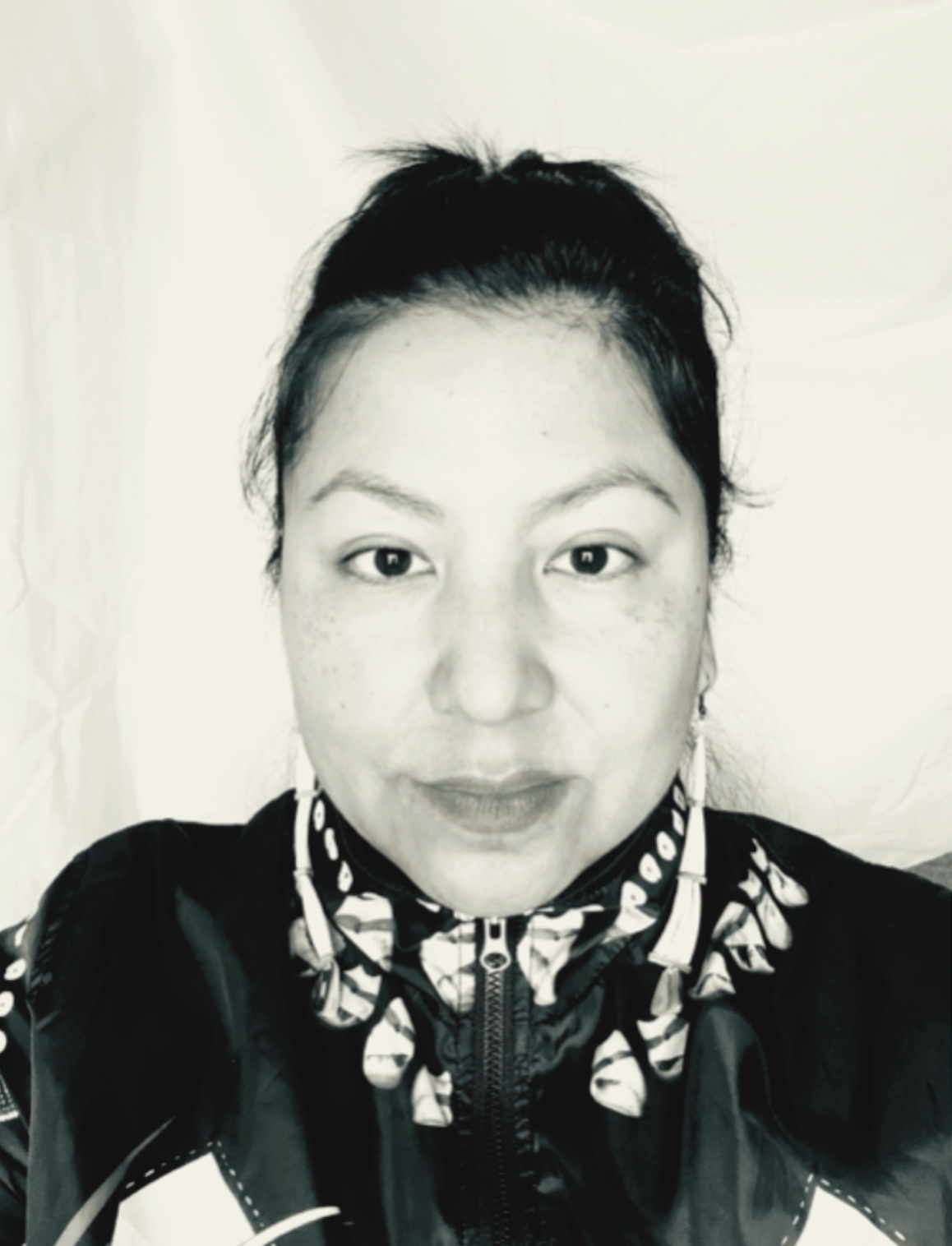 Black and white photo of a woman with dark hair pulled back, wearing a patterned high-collared jacket.