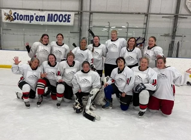 Group of women hockey players in white jerseys posing together on ice rink.