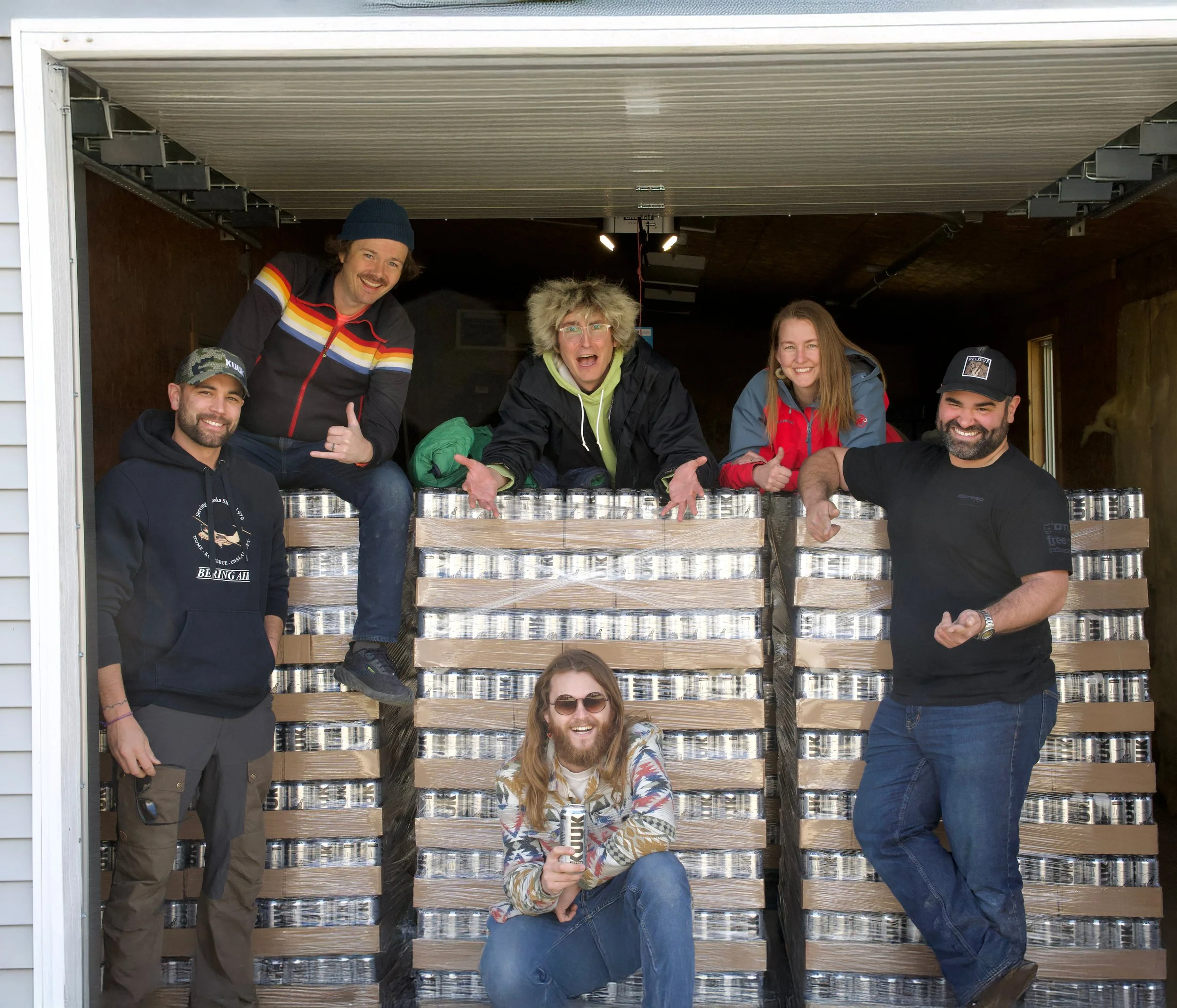 Group of six people posing in a truck with stacks of cans.